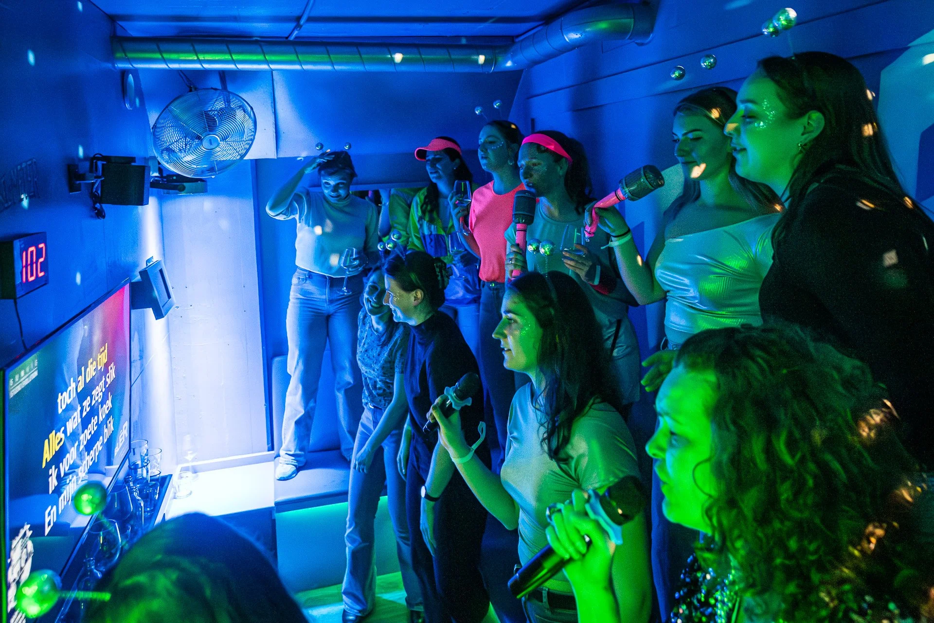 Een vergaderruimte met een grote vierkante houten tafel, omringd door comfortabele stoelen met leren zittingen, glaasjes water en notitieblokken met pennen. Grote ramen laten natuurlijk licht binnen.