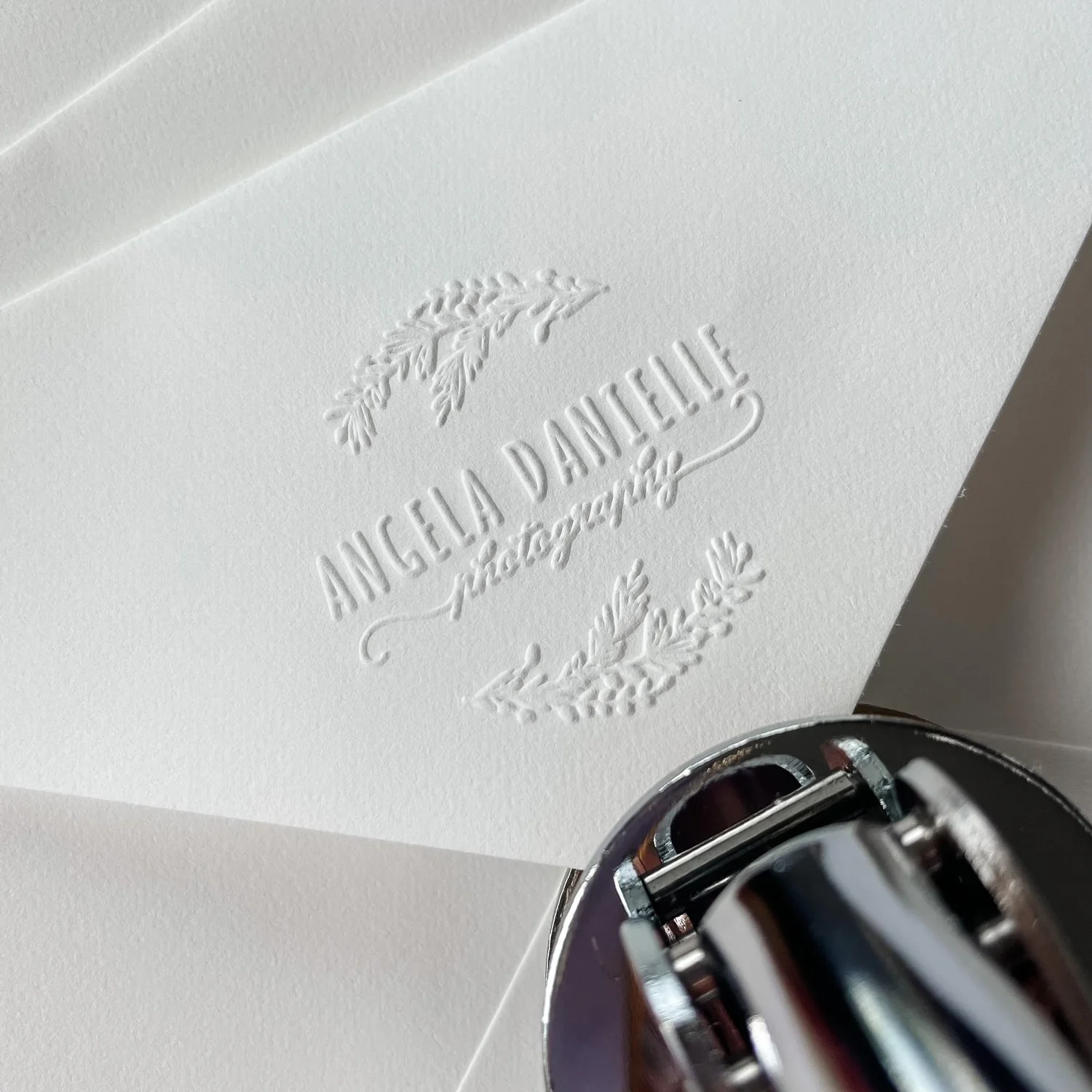 Triangle-flap envelope with Angela Danielle Photography logo embossed. Embosser at edge of frame.