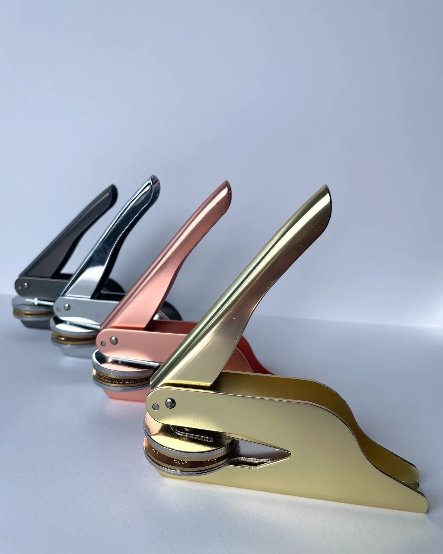 Four embossers side on to camera. Gold, rose gold, silver, and gunmetal against plain white background.