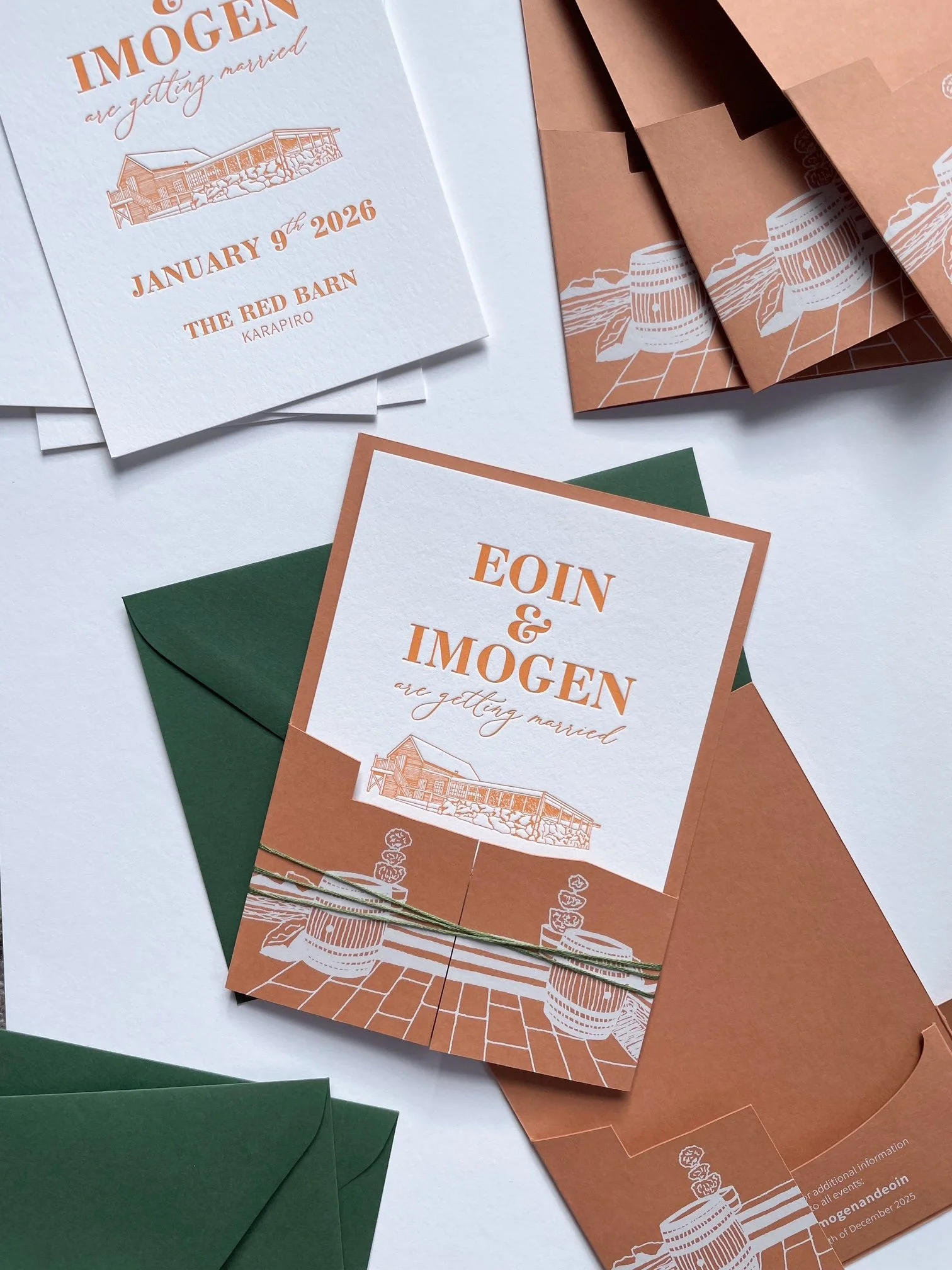 Wedding invitation cards with orange and white coloring, featuring illustrations of a barn, barrels, and pots of flowers, along with green envelopes.