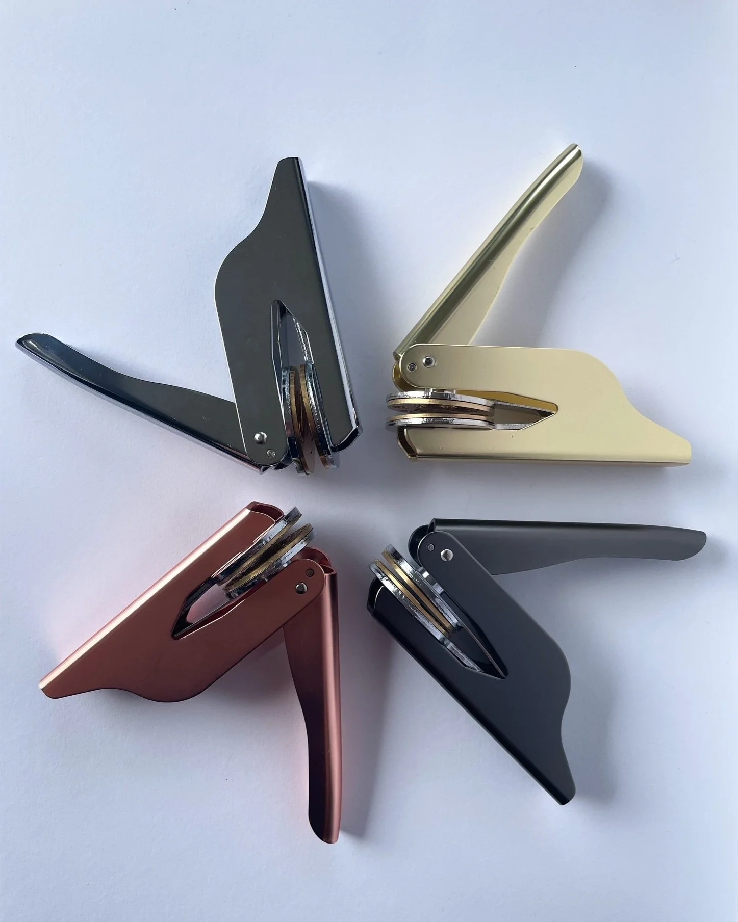 Overhead shot of four embossers laying in circle formation. Gold, rose gold, gunmetal, and silver against plain white background.