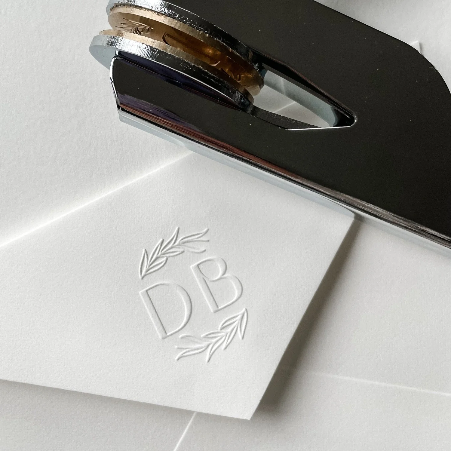 Overhead shot of gunmetal embosser laying against triangle-flap envelope embossed with 'DB' intials.