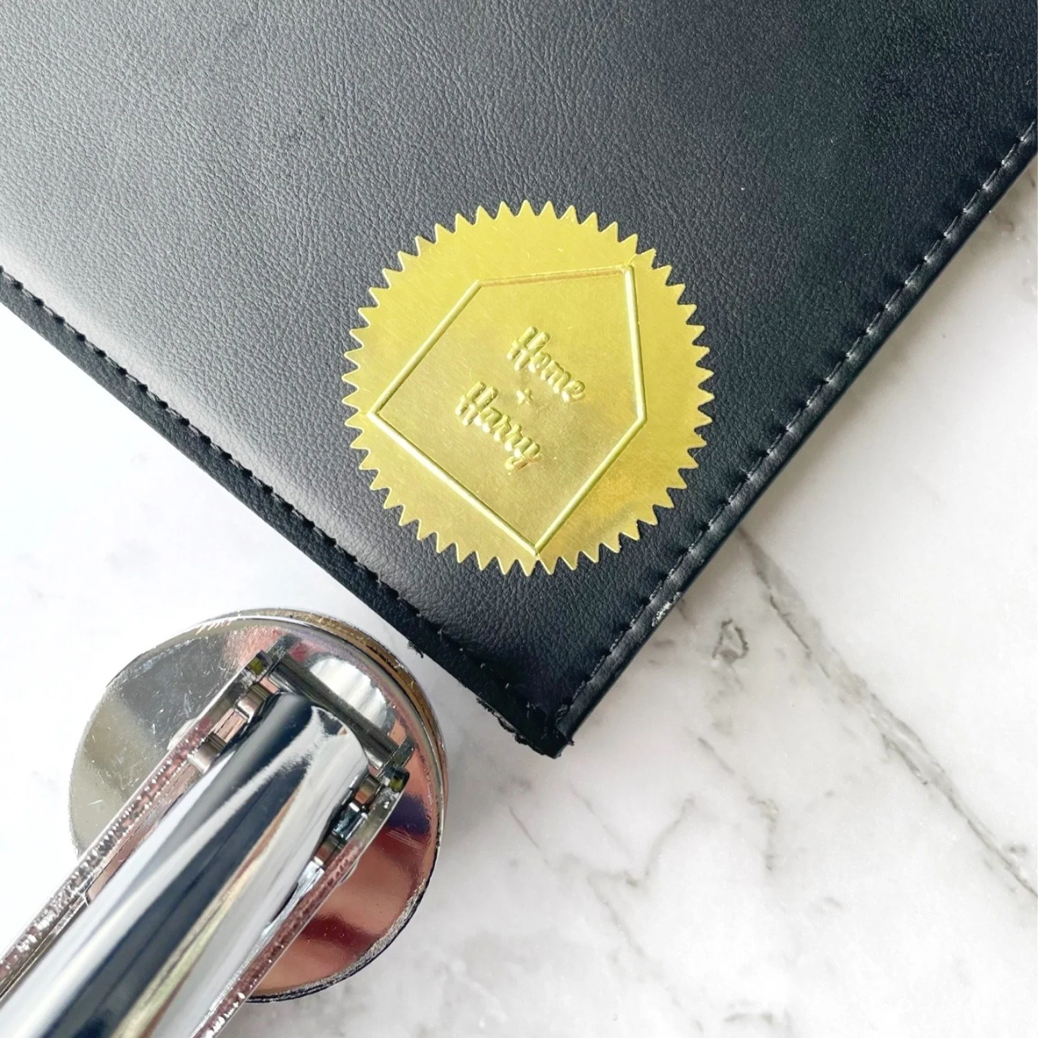 Edge of black leather cover with embossed gold foil sticker on. Embosser at edge of frame.