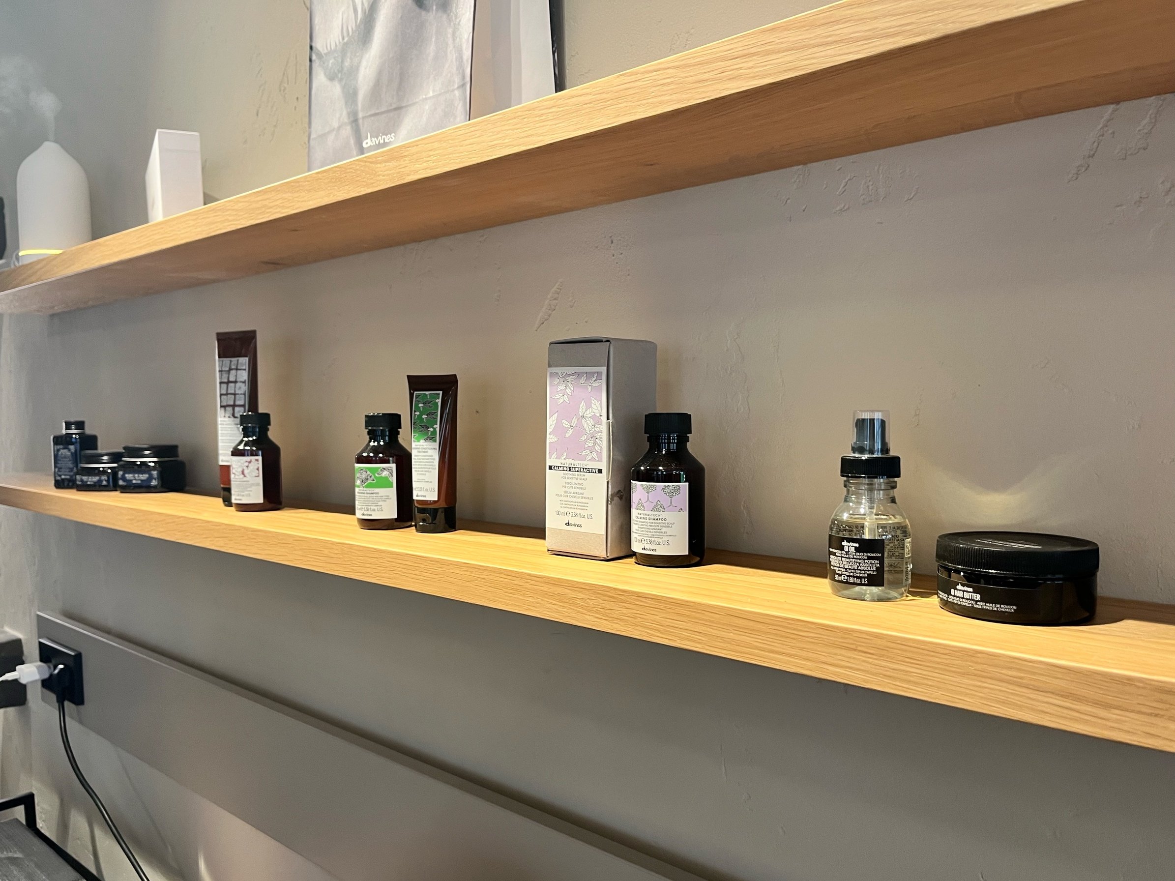 Regale mit verschiedenen Kosmetik- und Hautpflegeprodukten in Flaschen und Dosen, in einem Laden oder Spa. Hochwertige Produkte in dunklen und hellen Verpackungen, einige in Schachteln, auf Holzregalen montiert.