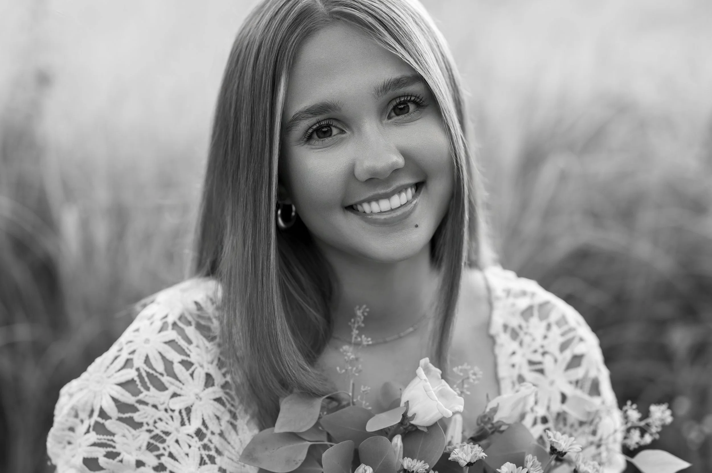 high school senior posing with flowers while sitting in a meadow for photos