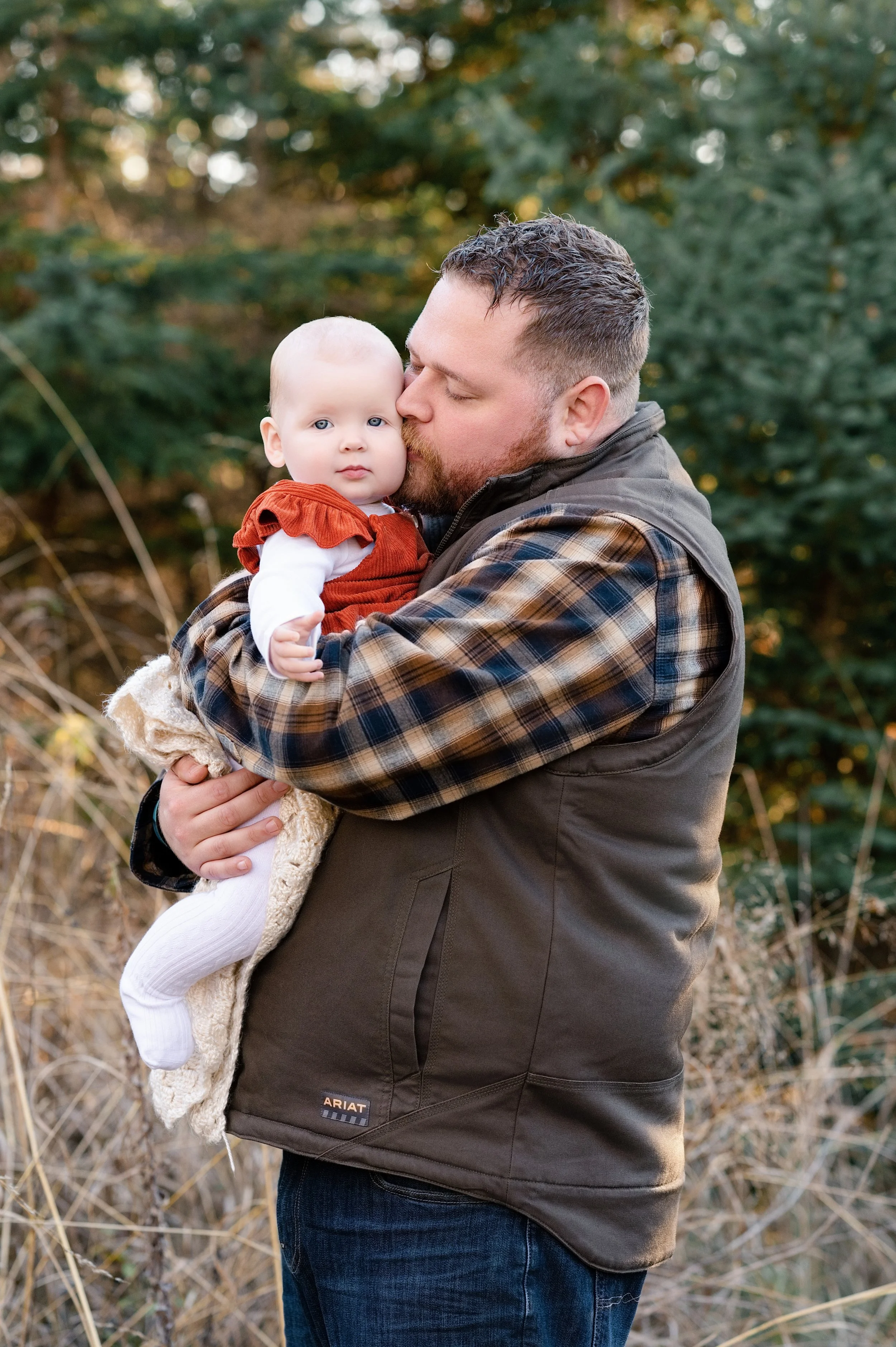 A man holding a baby girl outdoors with trees in the background.