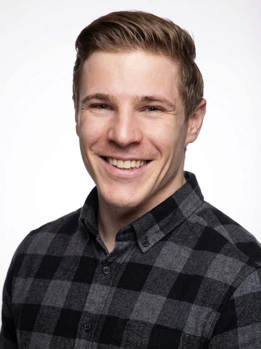 Junger Mann mit braunem, seitlich gescheiteltem Haar, lächelnd, trägt ein schwarzes und graues kariertes Hemd, vor weißem Hintergrund.