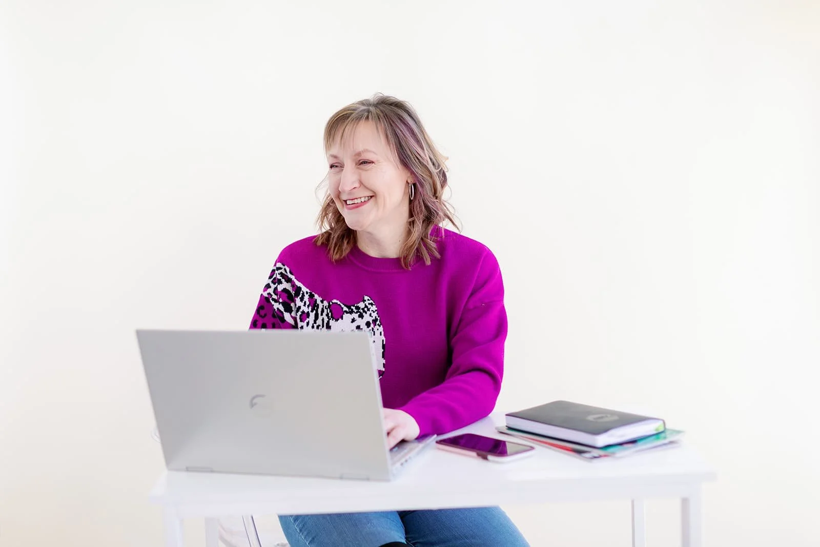 Jacki Hayes, a white woman in a hot pink sweater, is sitting at a desk working on a laptop.