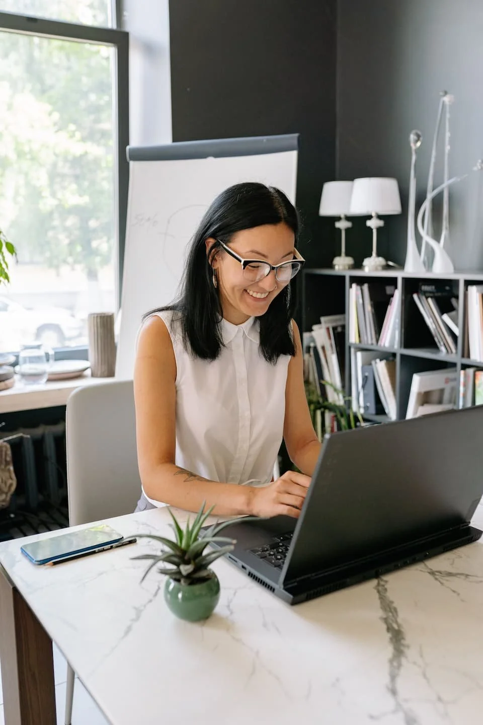 Woman with glasses, sitting out her computer smiling