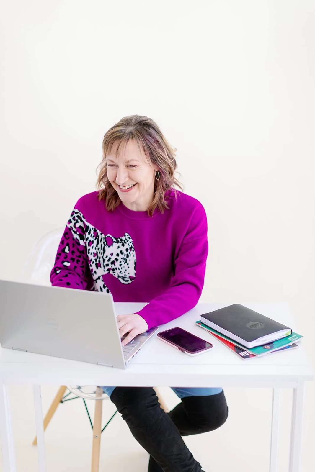 Jacki Hayes is sitting at a desk, smiling at an open laptop.
