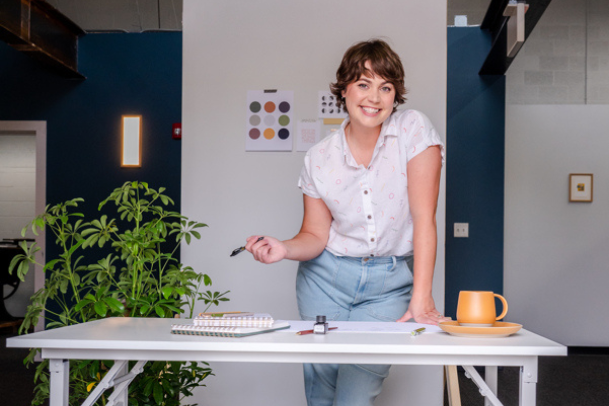 Mindy Carlson, a white woman with short hair, stands smiling in front of a craft table.
