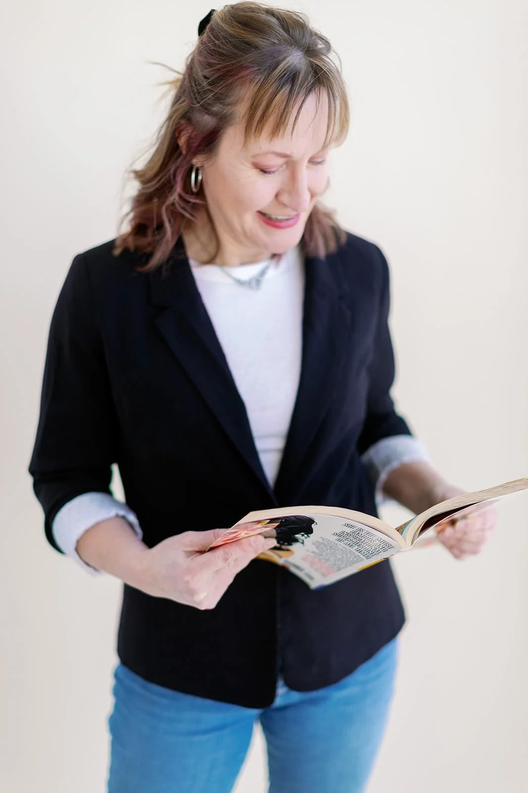 Jacki Hayes, a white woman, is standing while reading a Wonder Woman graphic novel. She is wearing a white shirt and black blazer.