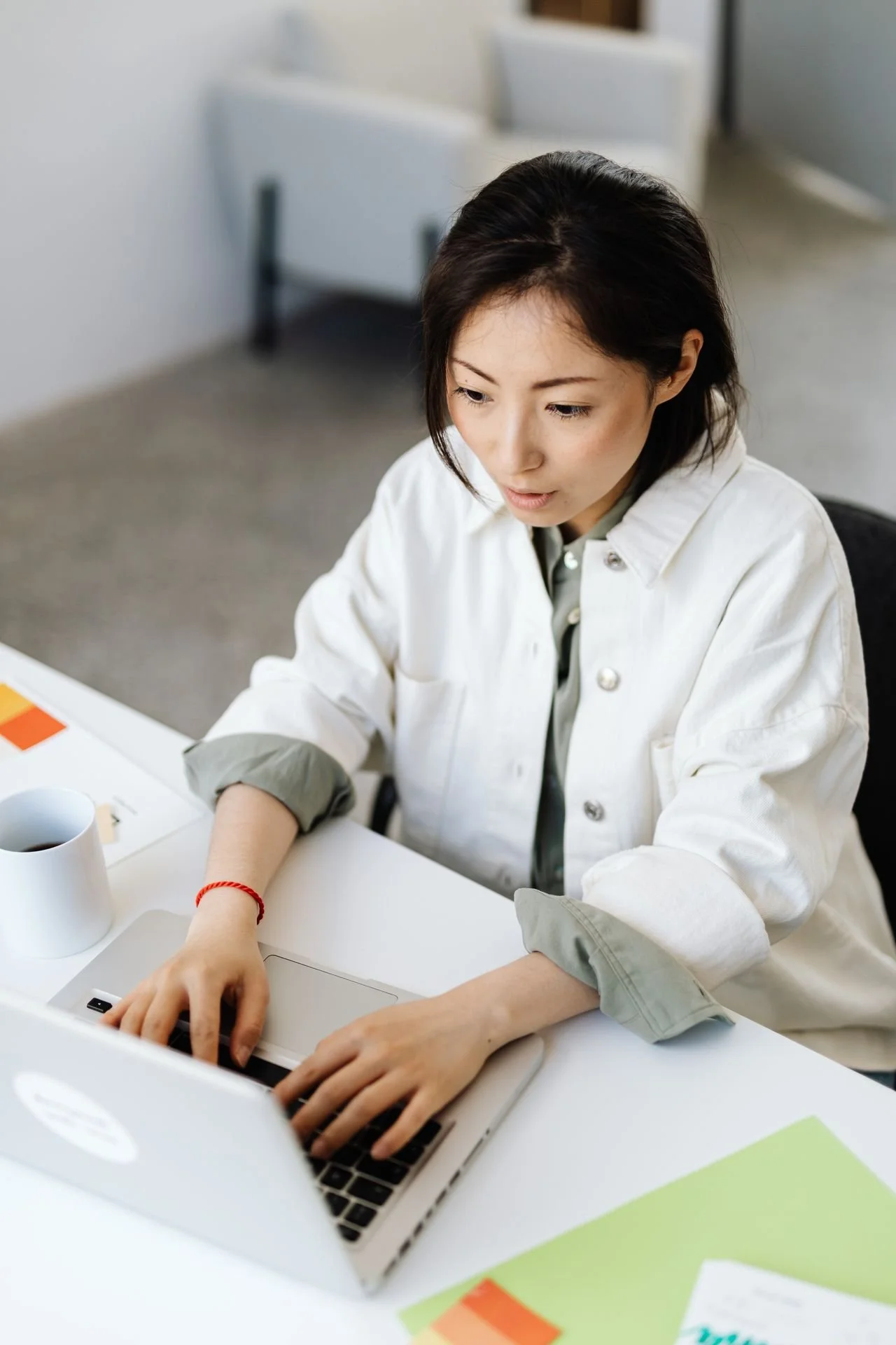 An Asian woman is sitting at a laptop working.