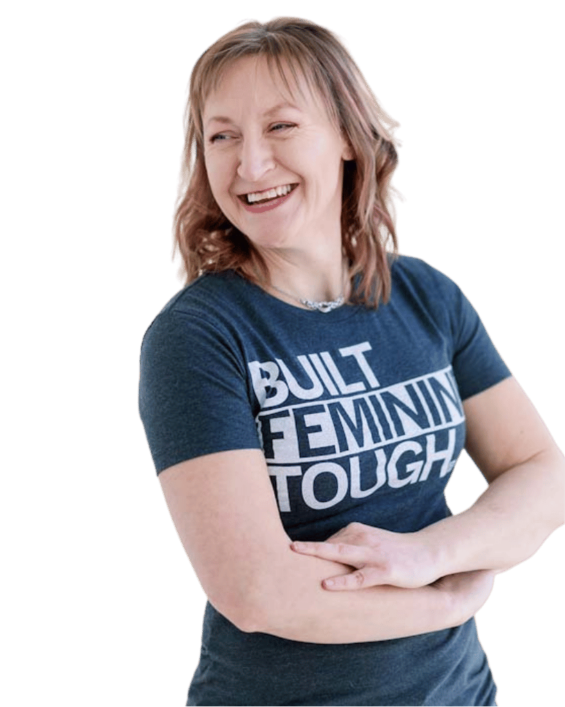 Jacki Hayes, a white woman with shoulder-length brown hair, is smiling with her arms crossed. She is looking over her shoulder and wearing a dark gray t-shirt.