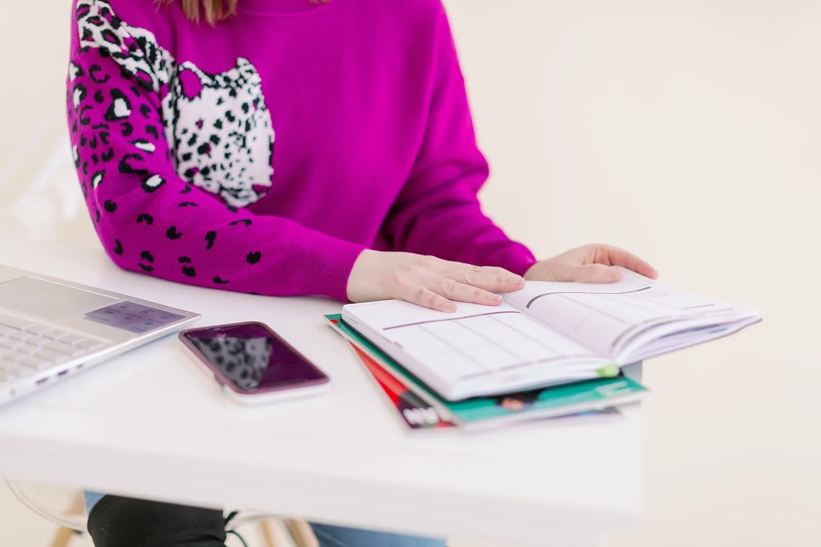 Close-up of Jacki's hands holding a planner open. She phone and laptop sit to her right.