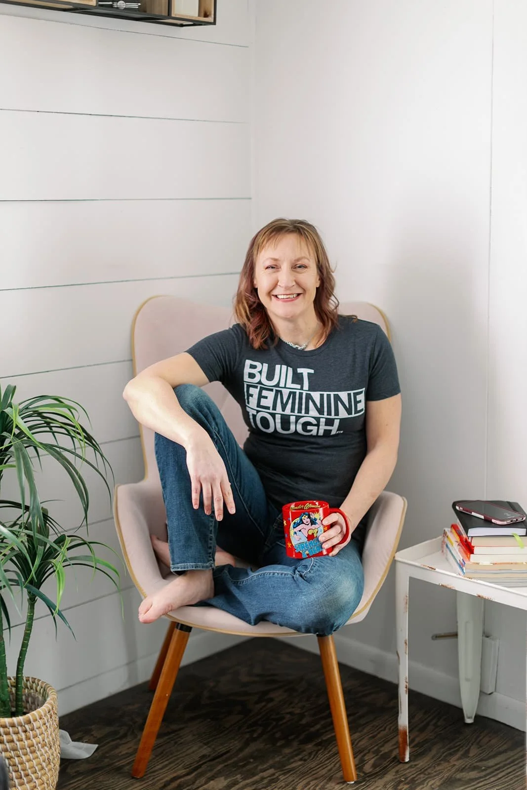 Jacki sitting in a modern arm chair with a Wonder Woman mug in her hand.