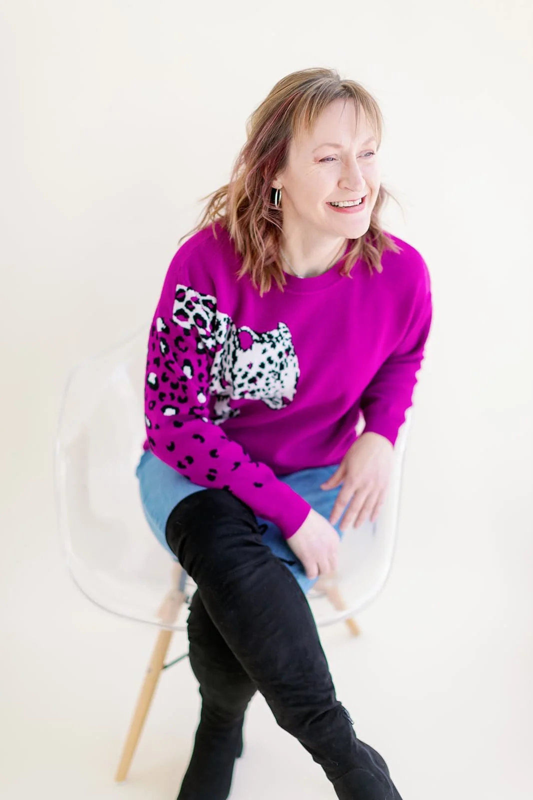System strategist, Jacki Hayes is sitting on a clear chair, wearing a hot pink sweater and jeans.