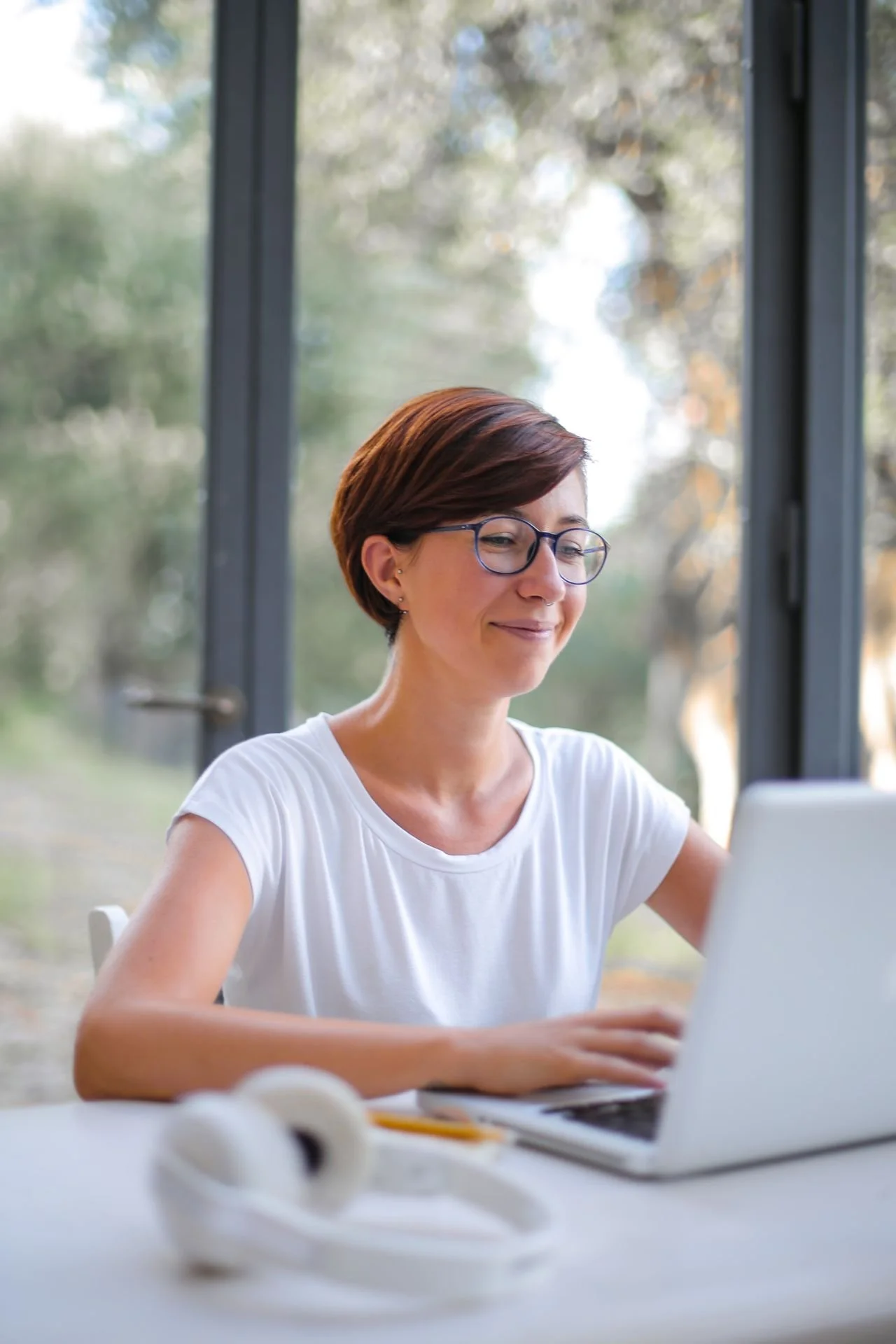 A white woman, with short brown hair is working at a laptop and smiling.
