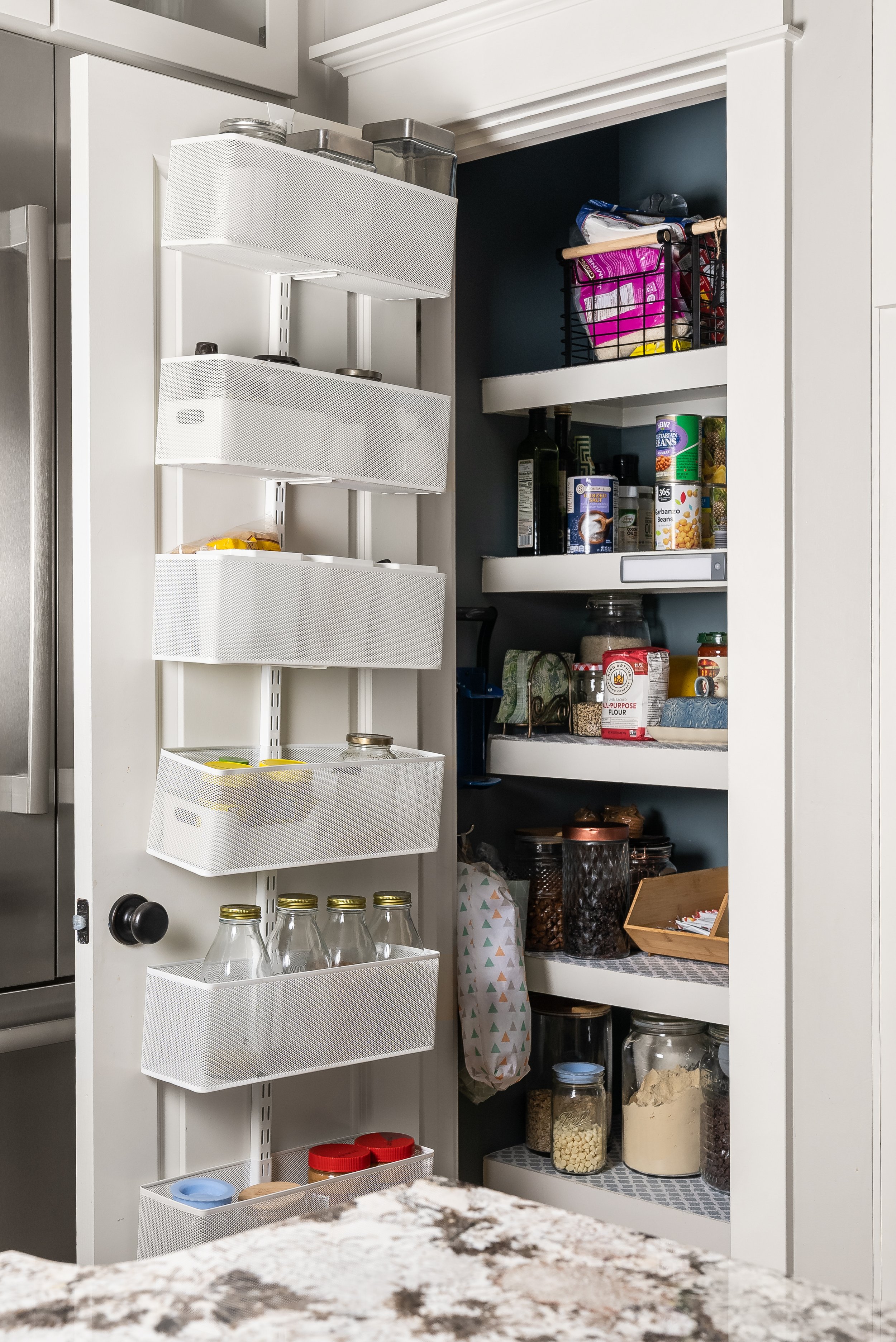 Eco-friendly pantry organization using reused glass jars for dry goods and an Elfa over-the-door organizer to maximize storage in a small pantry.