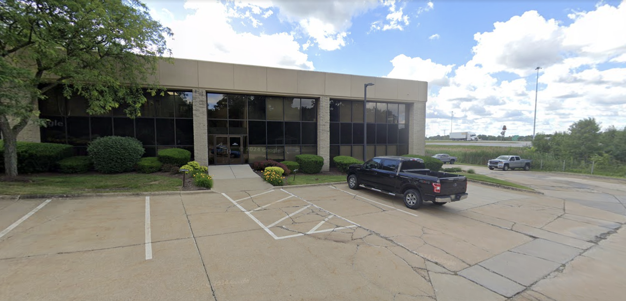 A two-story building of tan stone with large groups of black windows. 77 is visible to the right.