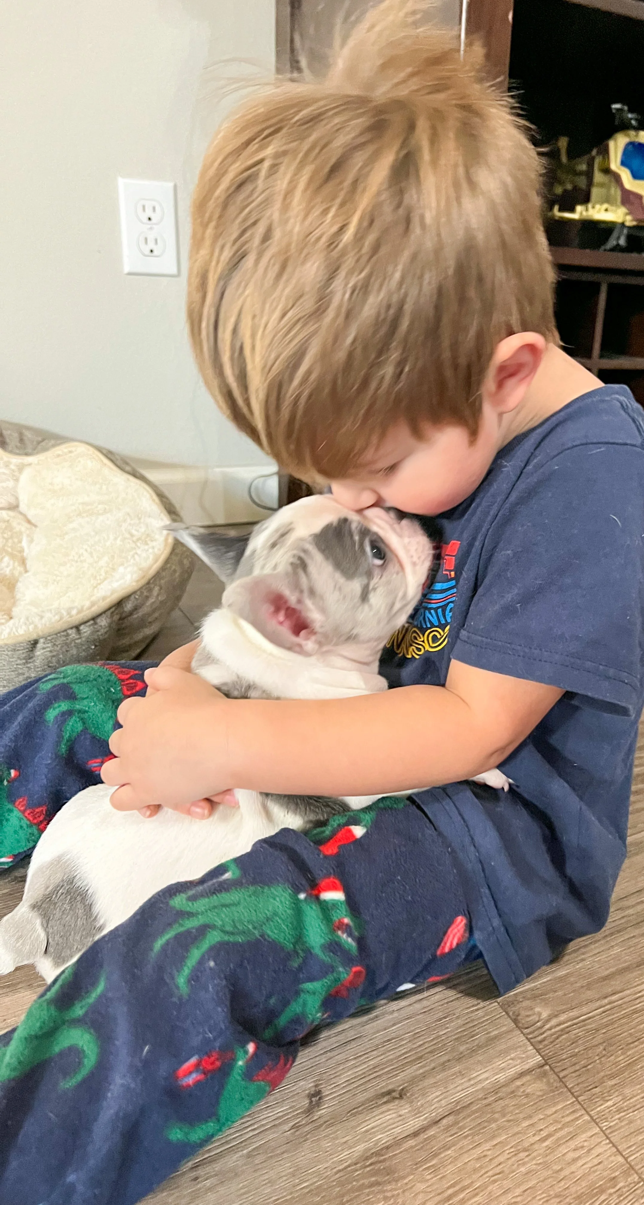 Outdoor wedding reception setup with a long white table decorated with greenery and candles, hanging paper lanterns and string lights overhead, and surrounded by trees.