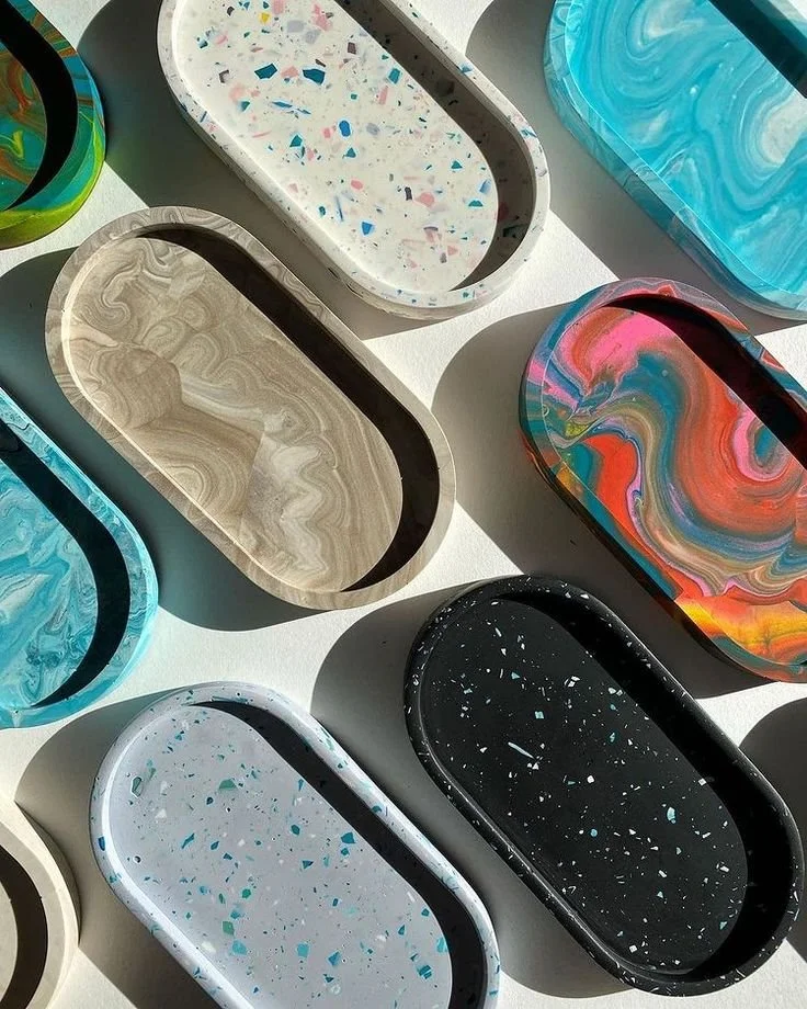 Colorful terrazzo-style oval trays with various patterns and colors, including blue, black, white, and multicolor, arranged on a light surface.