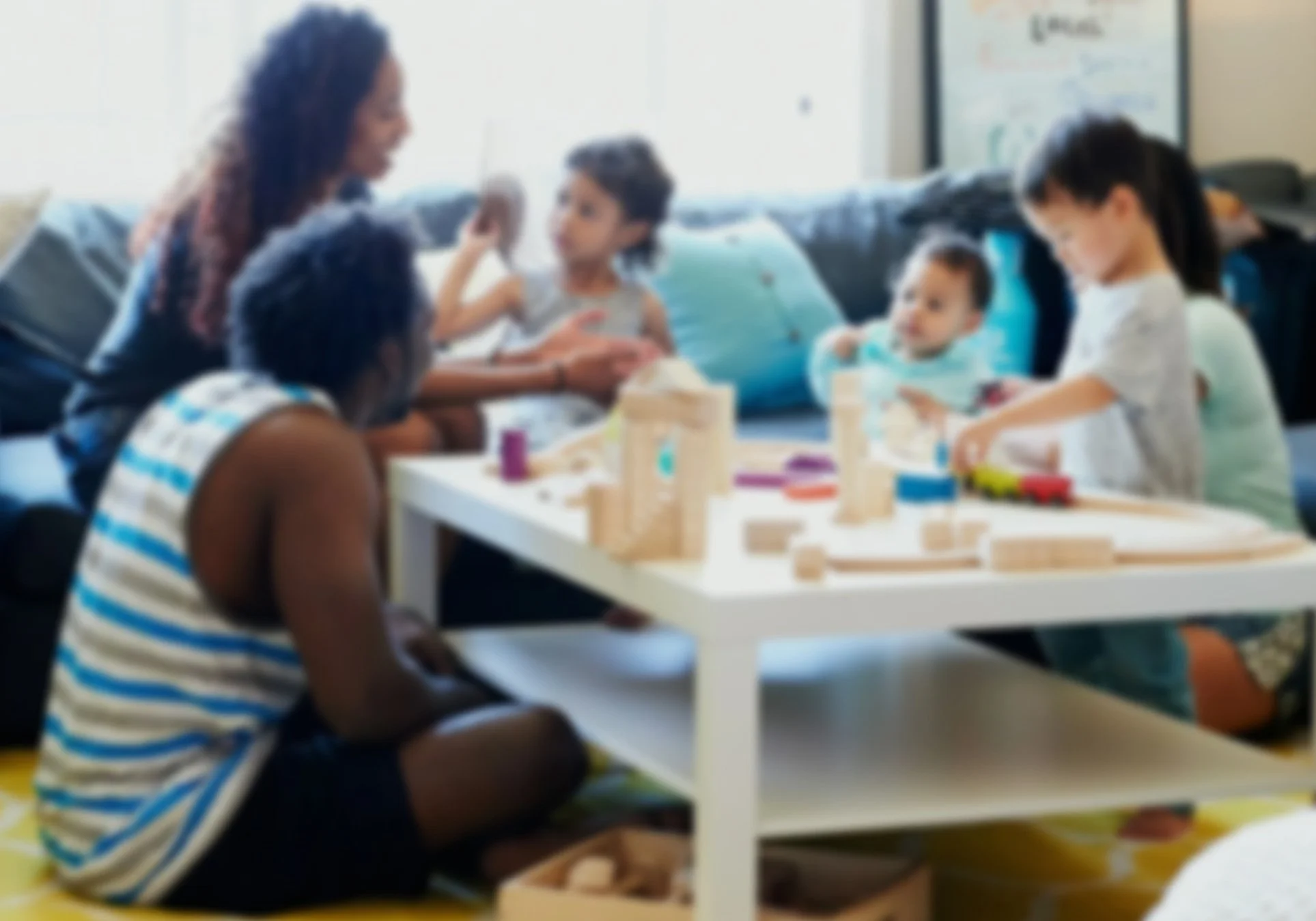 Children and two adults sitting at a white table playing with wooden blocks in a living room.