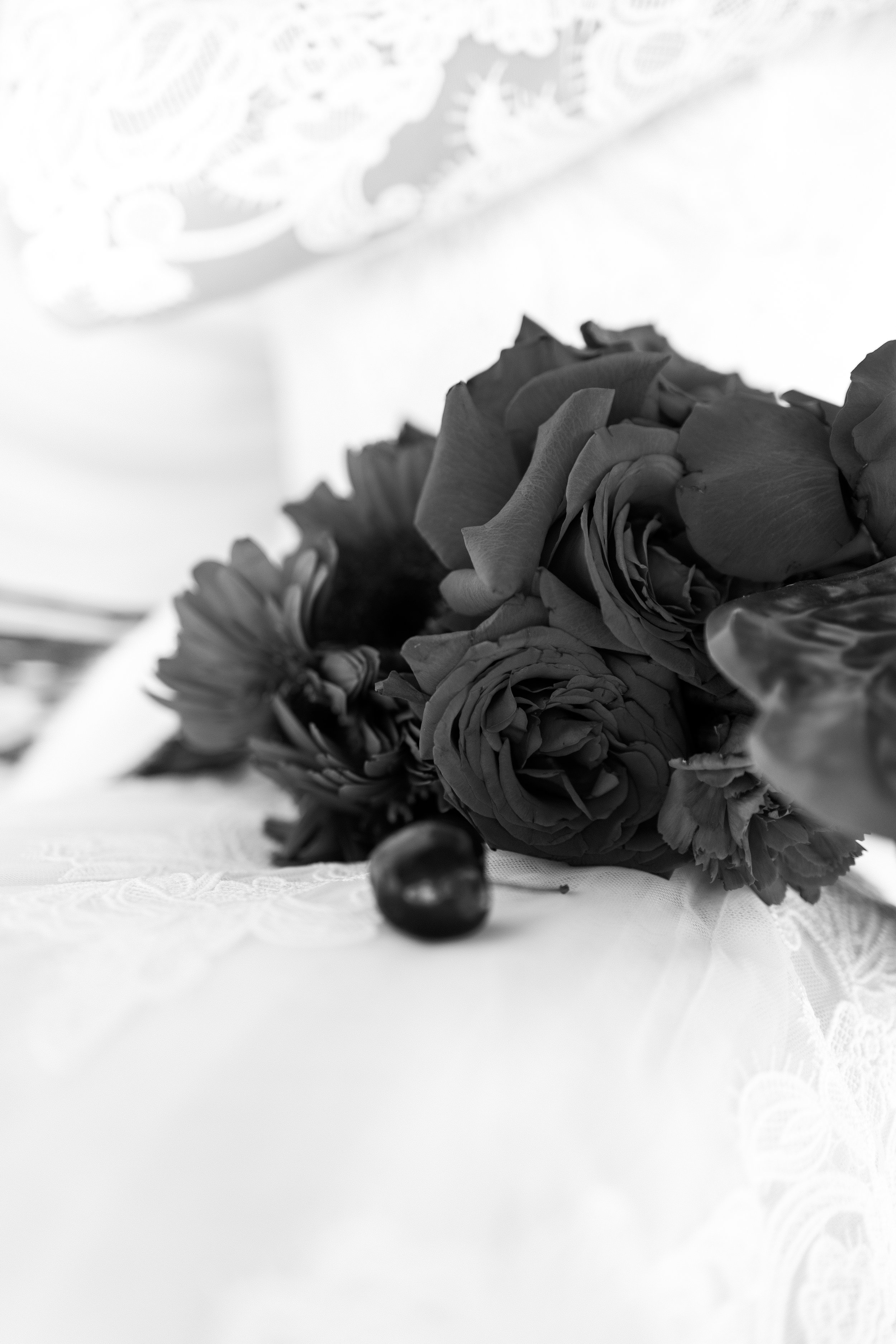 A black and white photograph of a bouquet of roses and a cherry placed on a lace tablecloth