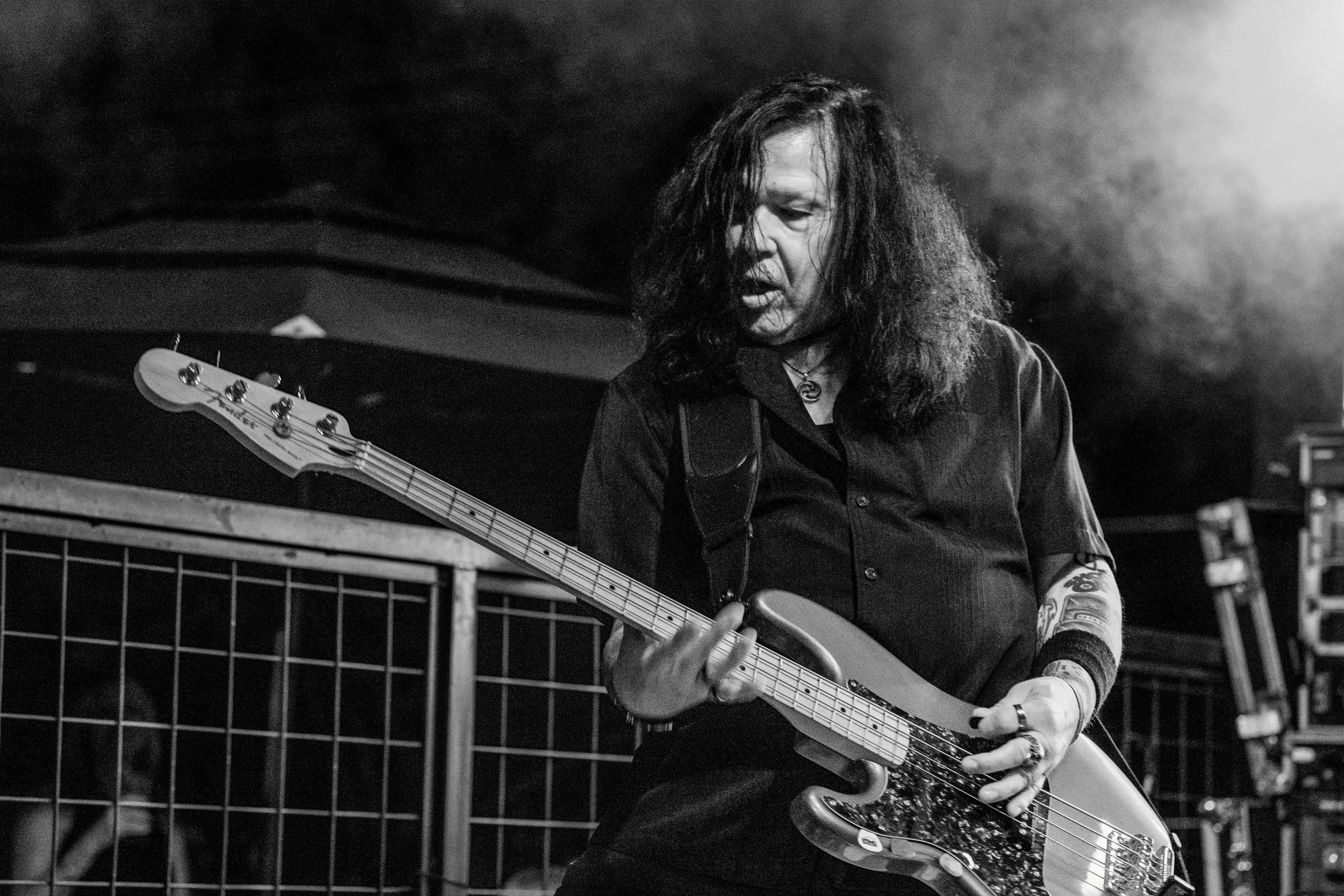 Guitarist of Shotgun Opera playing an electric guitar, with long hair covering part of their face, in a dimly lit setting with smoke or mist in the background.