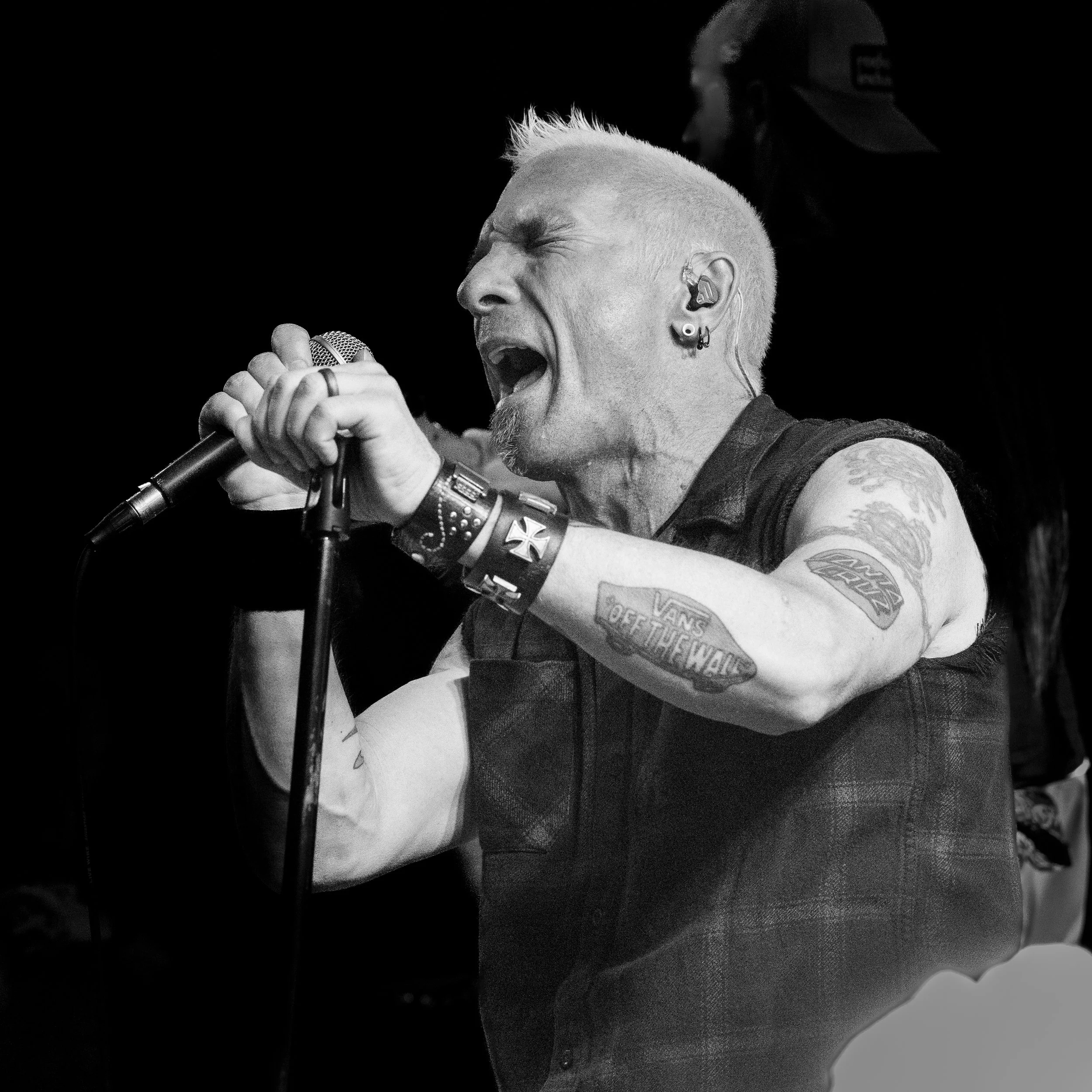 Black and white image of front man of Shotgun Opera singing into a microphone with closed eyes and an emotional expression, wearing a sleeveless shirt and wearing earrings.