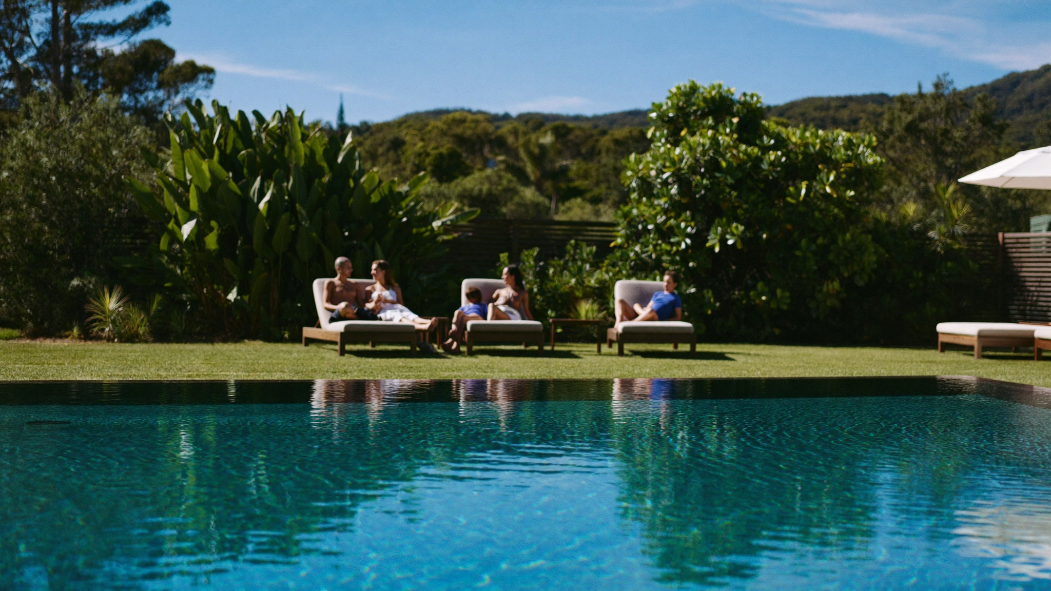 Clear pool water in a Gold Coast backyard in spring, family relaxing poolside