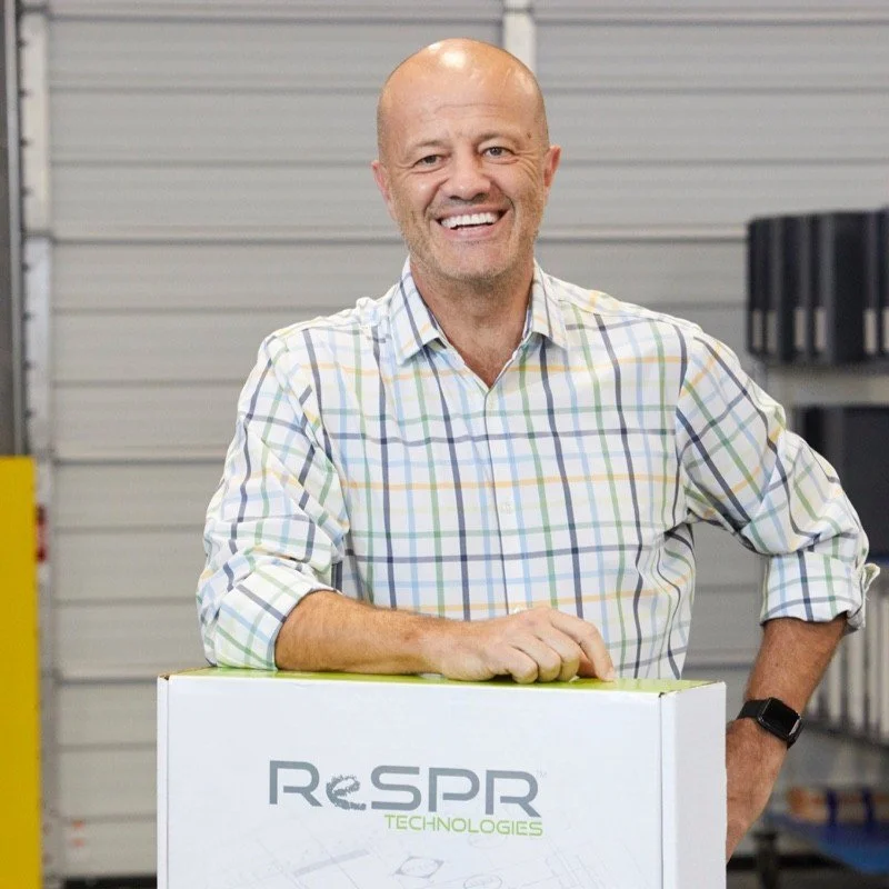 Smiling man in plaid shirt standing in warehouse with a box labeled ReSPR Technologies.