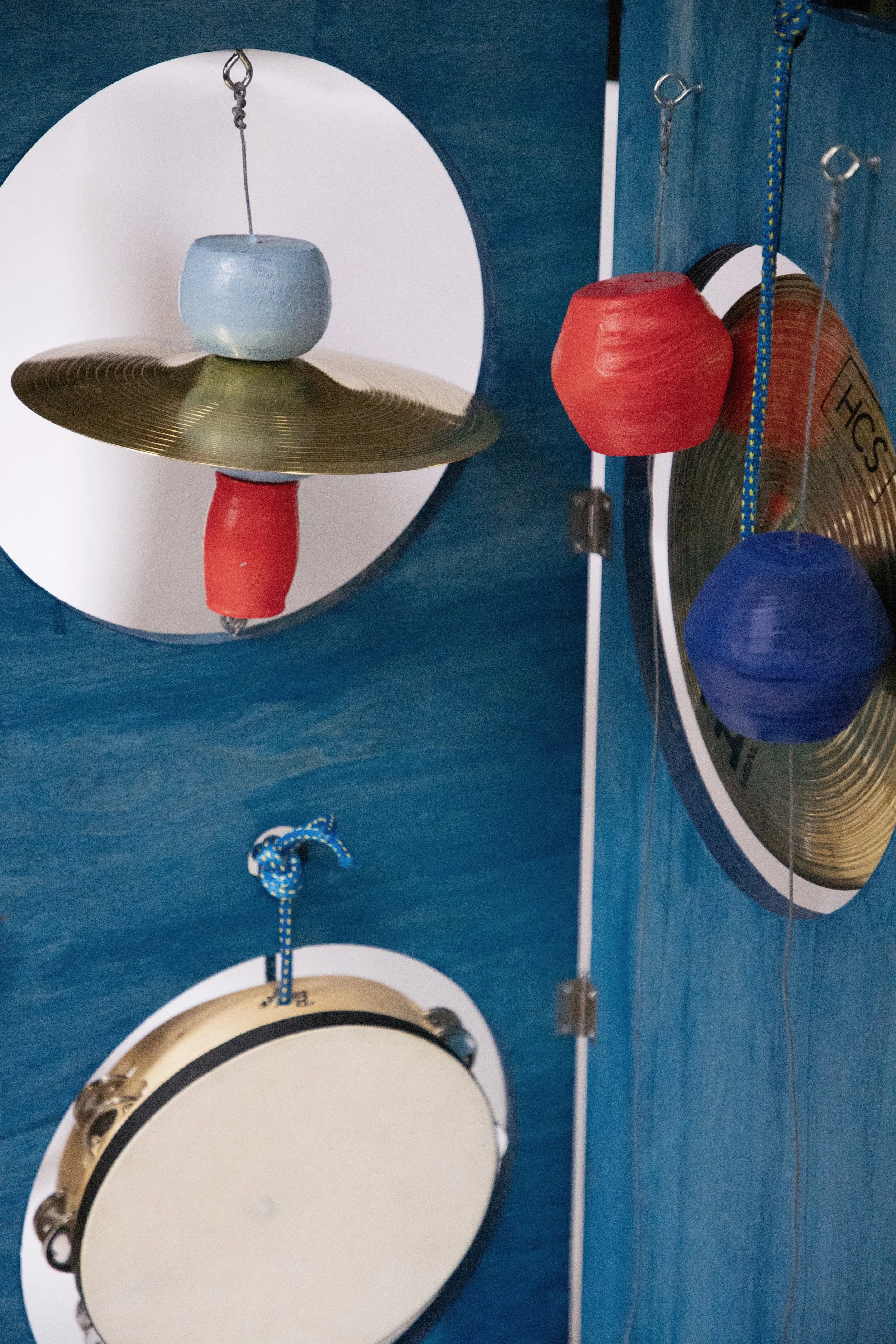Percussion instruments including cymbals, maracas, and a tambourine hanging on a blue wall with a mirror