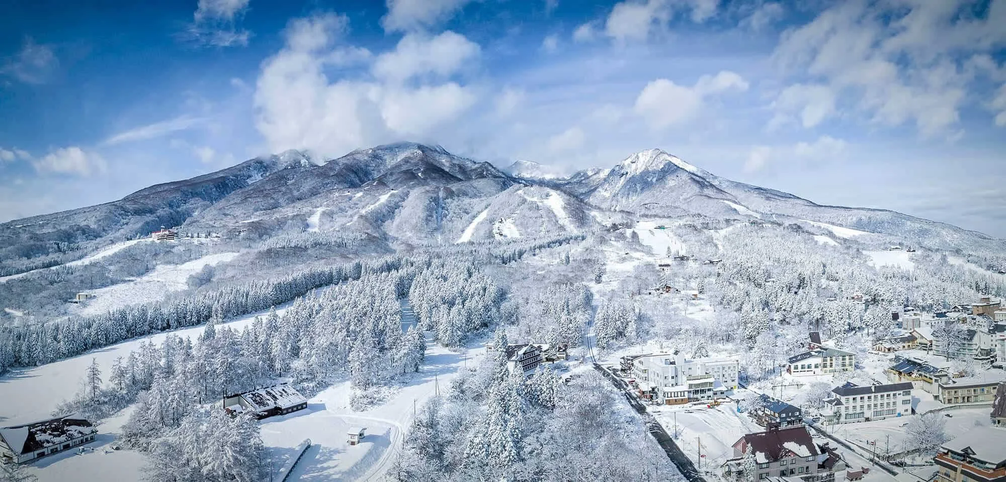 Snow-covered mountains with a partly cloudy sky and a town at their base.