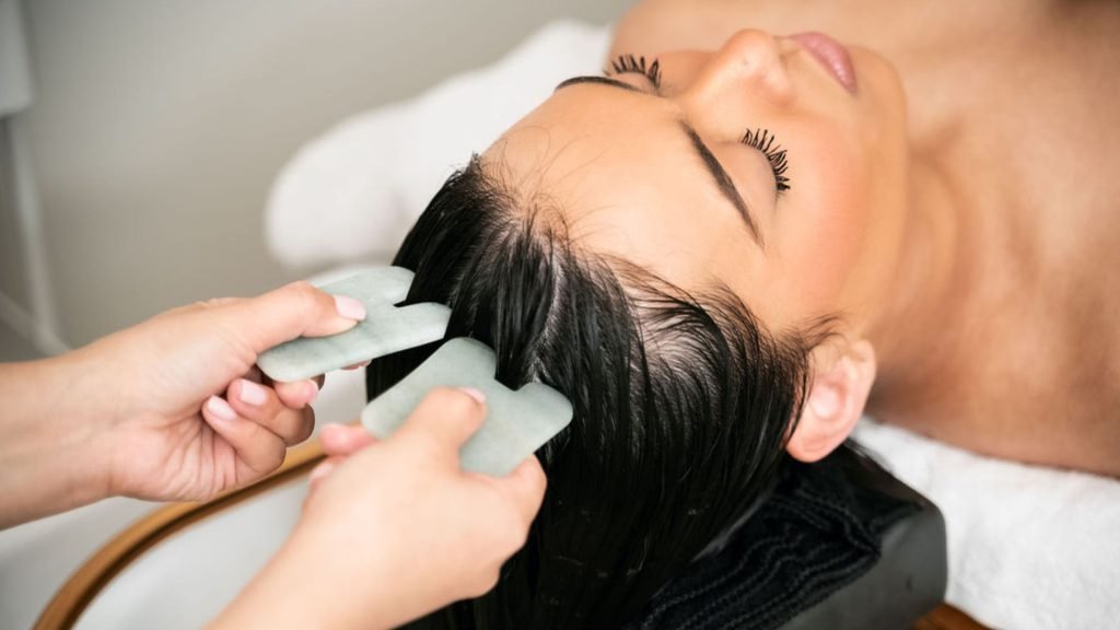 Person receiving scalp massage with stone tools in a spa setting.