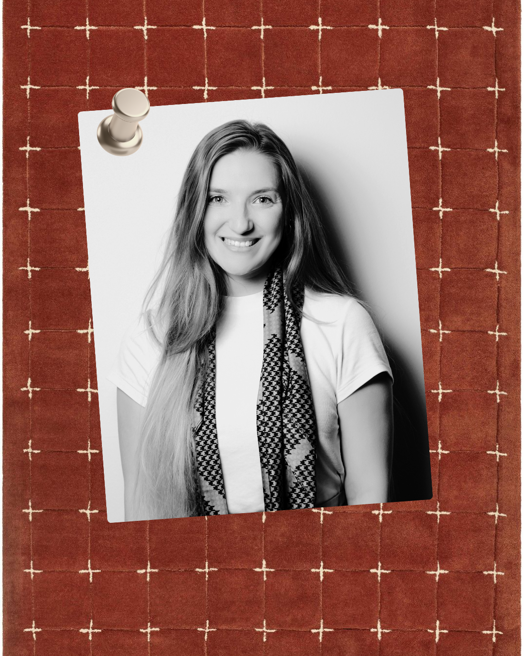 Black and white portrait of a smiling young woman with long hair, wearing a patterned scarf and a white t-shirt, pinned to a red grid-patterned corkboard.