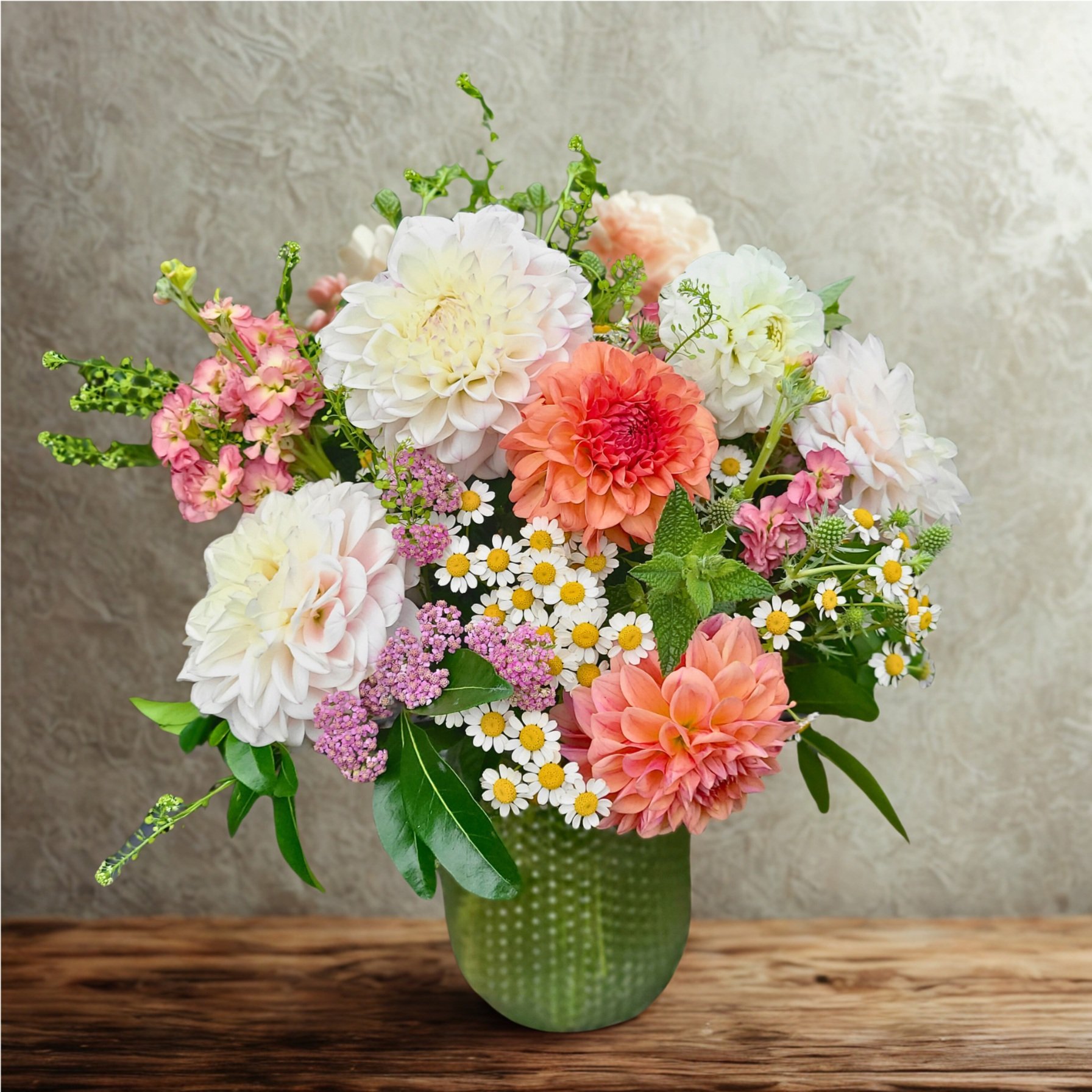 A white vase with a floral arrangement of pink and white roses, red peonies, green leaves, and eucalyptus branches.