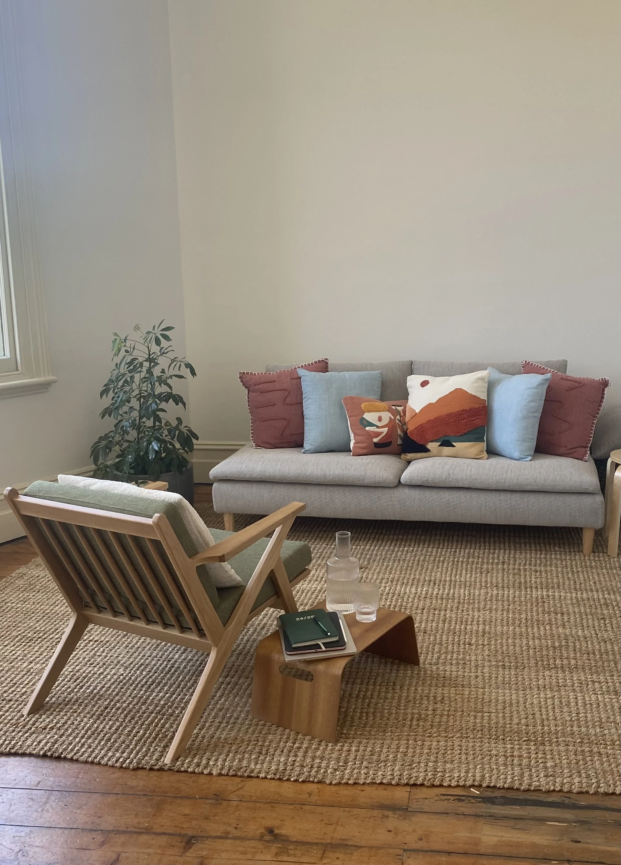 Sonia Dempsey's therapy room at Stable Health in North Fitzroy. A grey couch with cushions in shades of blue and ochre and a wooden chair with olive green upholstery