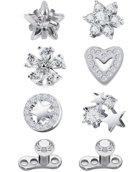 Collection of silver jewelry and charms, including snowflake-shaped pendants, a heart-shaped pendant with a heart and circular stones, a circular charm with a star and sparkling stones, star-shaped charms with stones, and metal beads with clear stones.