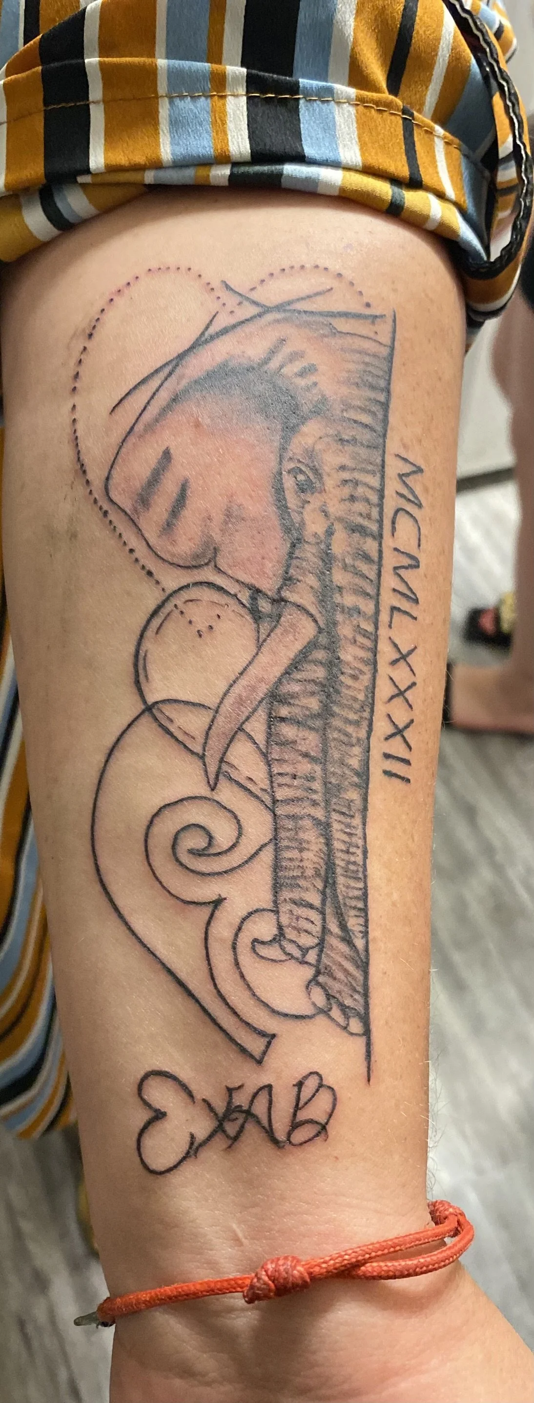 Tattoo of an elephant with a swirling pattern, Roman numerals MCMLXXXII, and initials EAB on a person's leg.