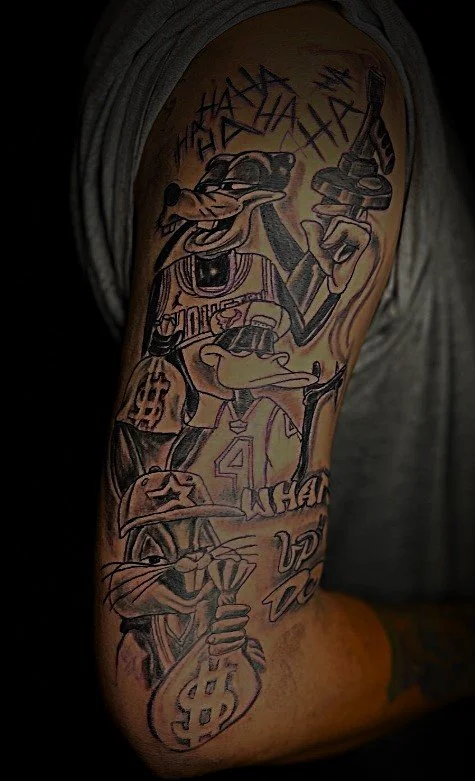 Tattoo of cartoon characters with guns and money on an arm
