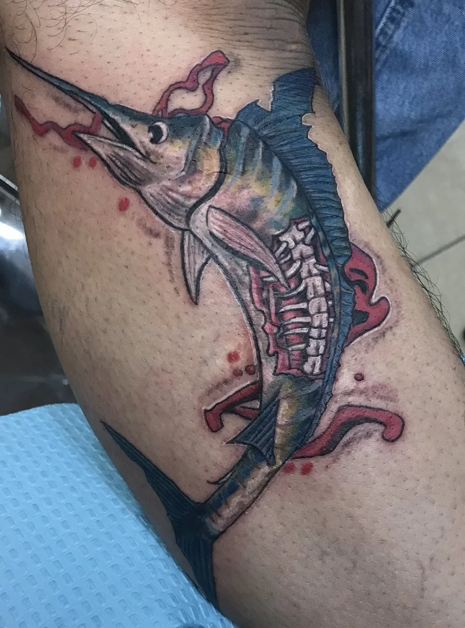 Colorful tattoo of a marlin fish with visible anatomy details on a person's arm.