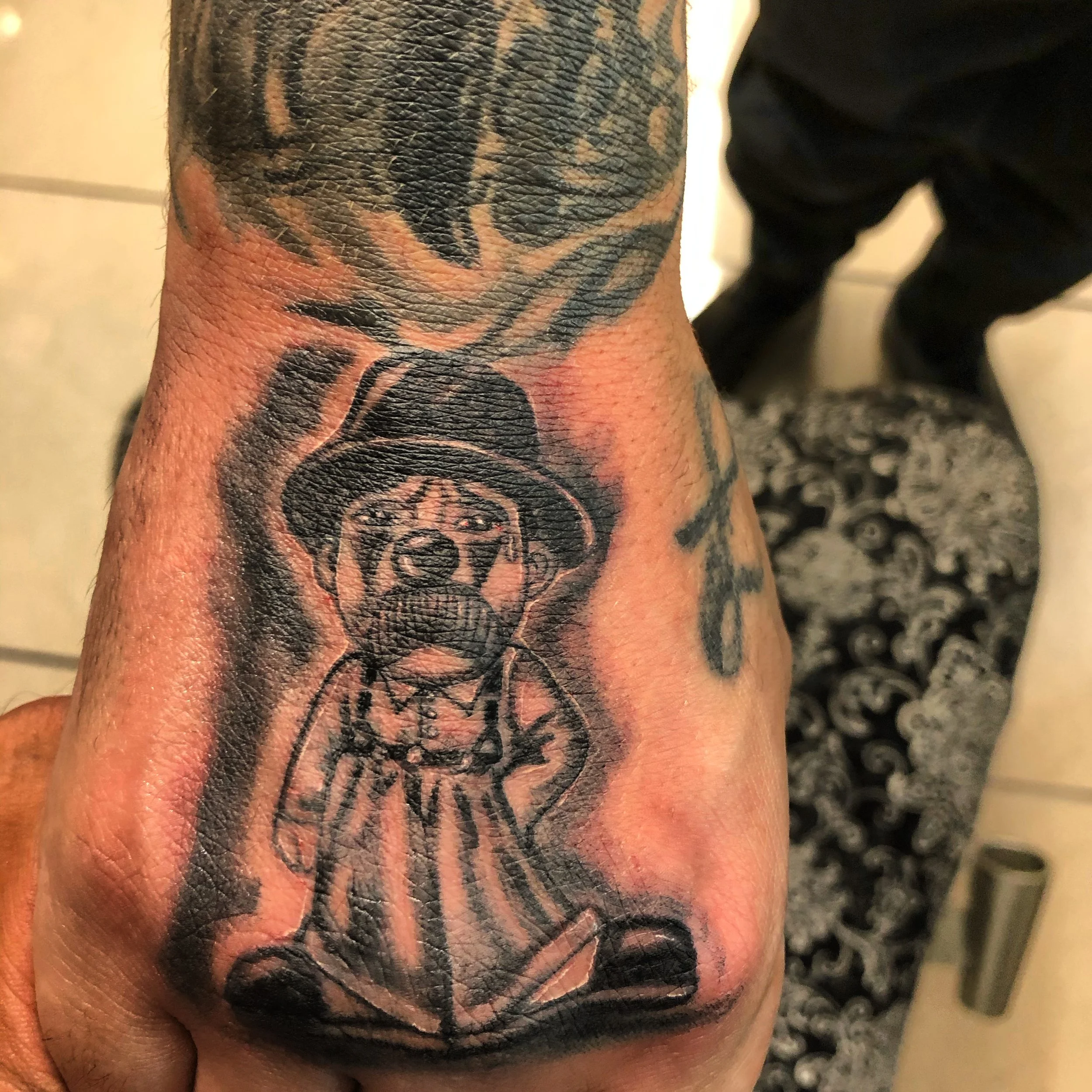 Close-up of a hand tattoo depicting a cartoonish figure in a suit and hat.