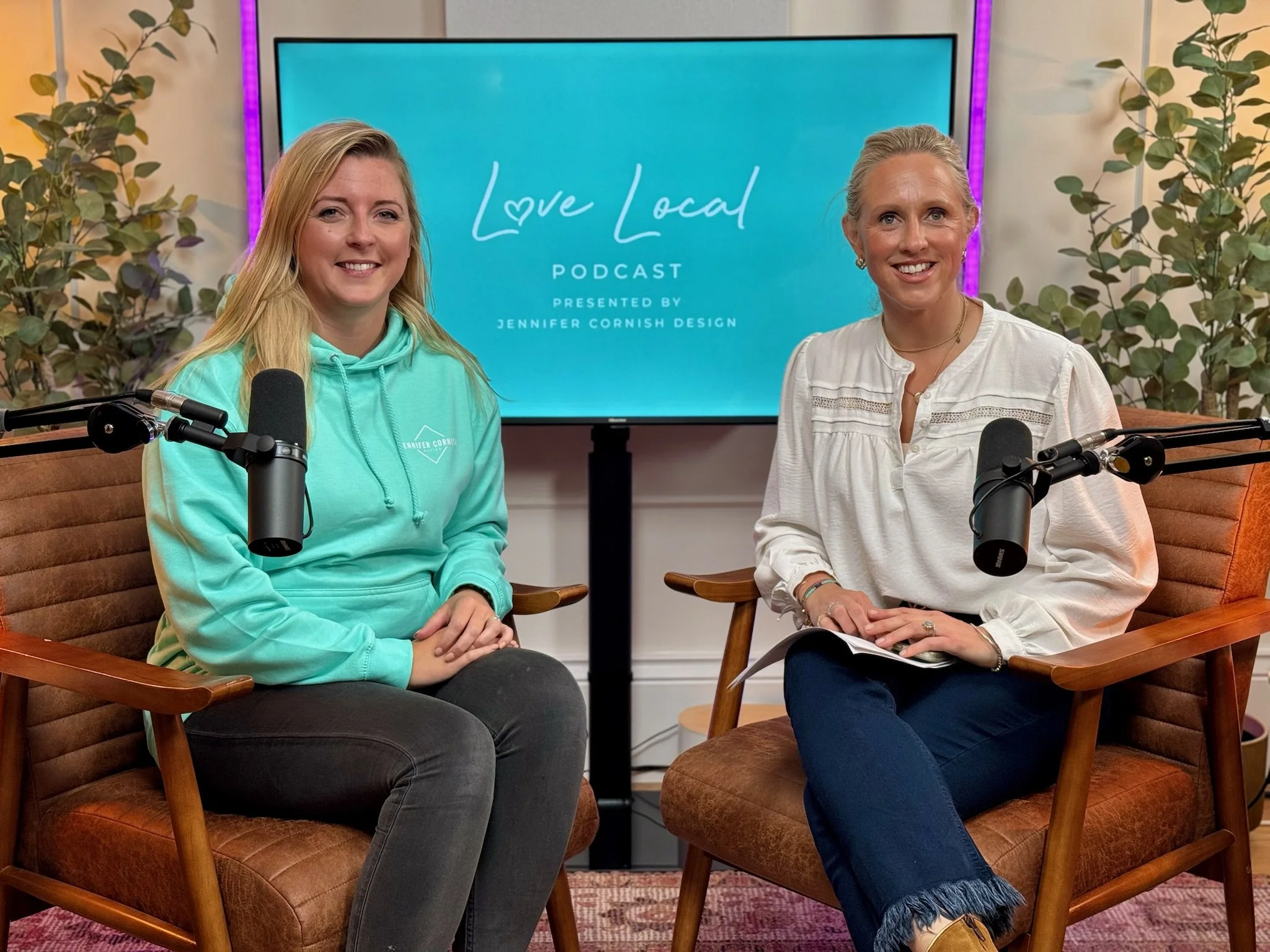 Two women sitting in armchairs with microphones, recording a podcast titled 'Love Local' presented by Jennifer Cornish Design, with a screen behind them displaying the podcast title.