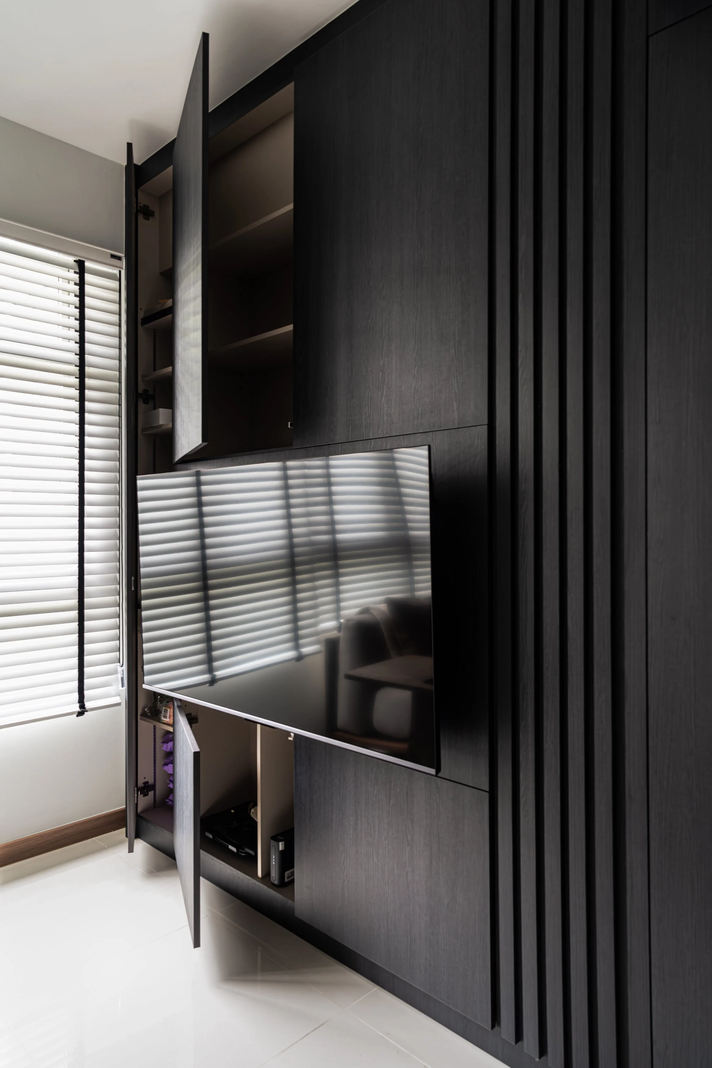 Sleek, full-height black cabinetry with fluted panels and integrated TV storage in a modern couple abode, demonstrating seamless storage solutions in interior design Singapore.
