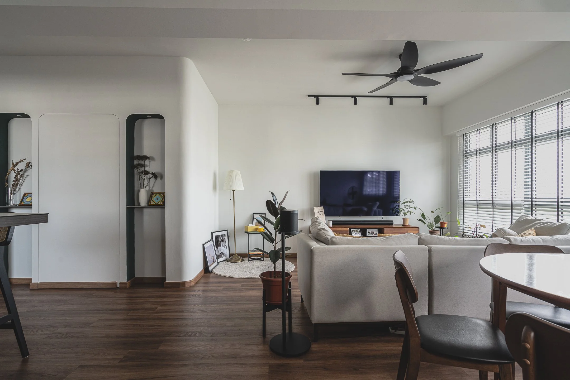 A spacious and airy couple abode living room featuring a curved white partition wall with built-in niches, dark wood flooring, and a minimalist interior design Singapore aesthetic.