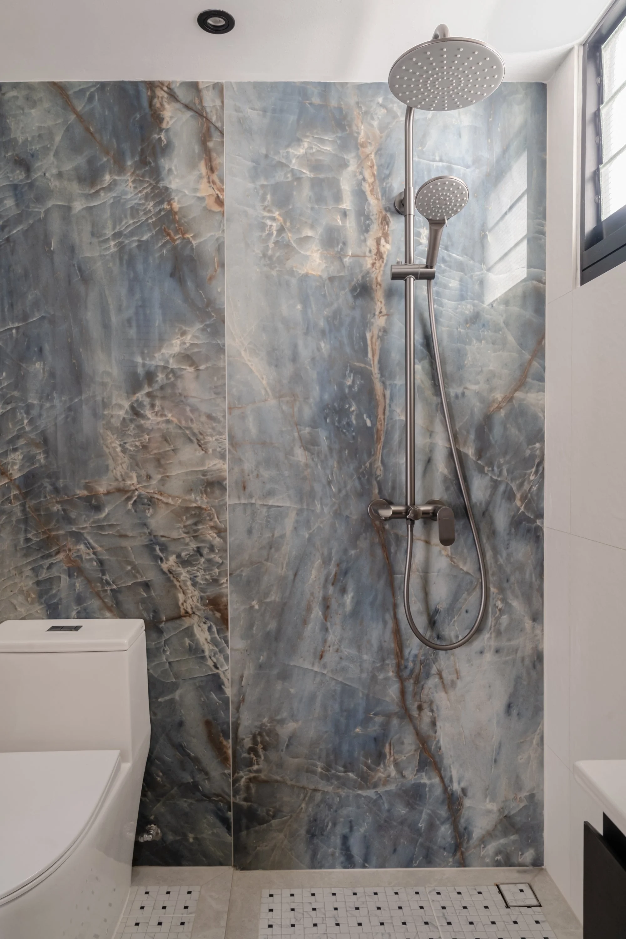 Contemporary bathroom with striking blue marble-effect shower wall and stainless steel rain shower set.