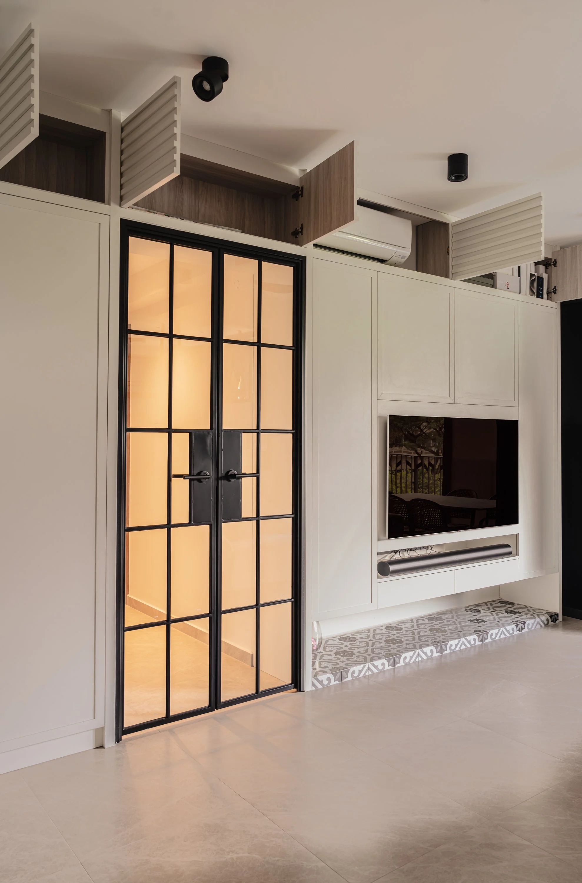 Expertly planned interior design Singapore in a couple abode, featuring integrated white built-in storage that cleverly hides an air-conditioning unit and maximizes vertical space alongside elegant black-framed glass double doors.