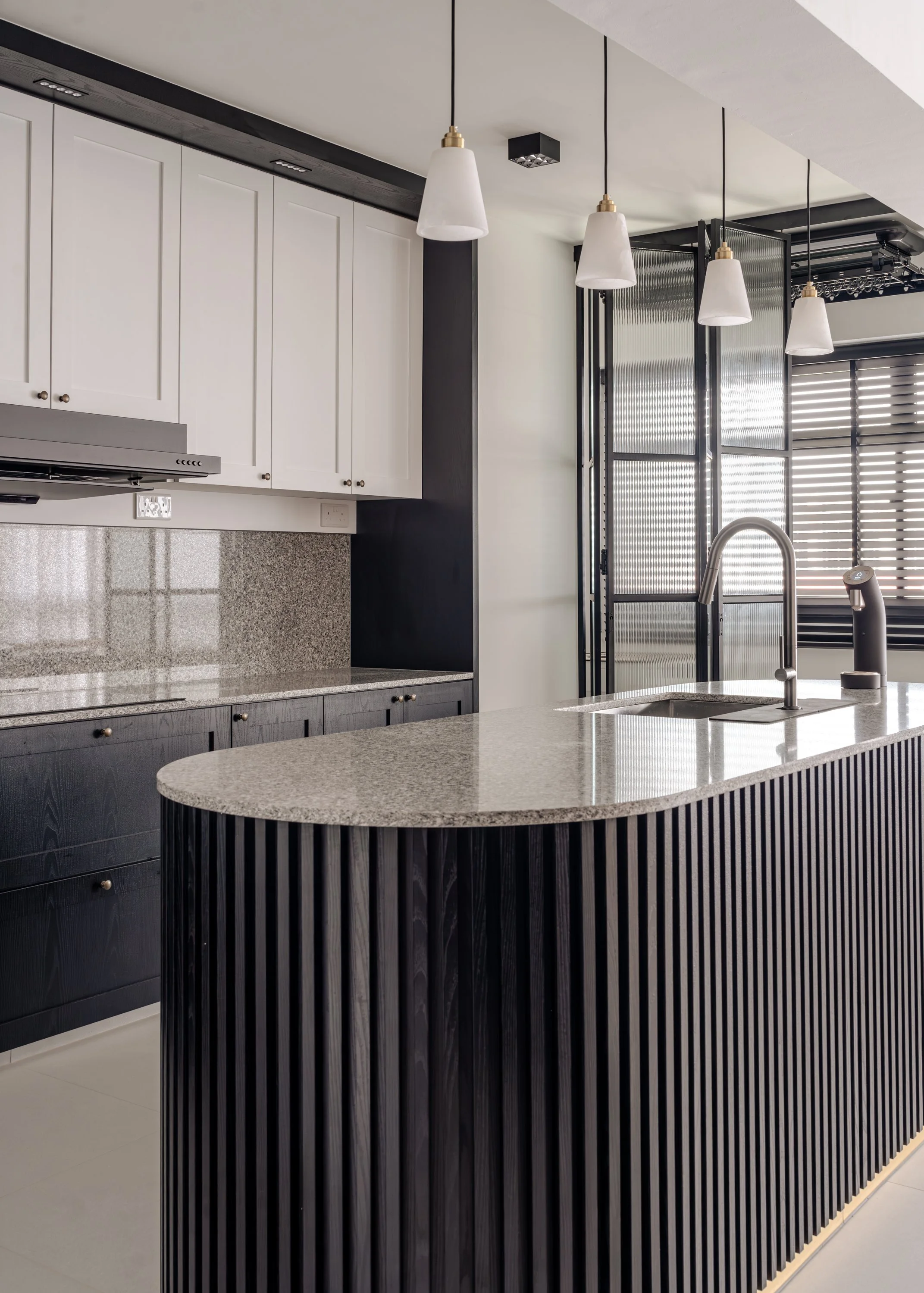 Modern kitchen with black fluted island, granite countertop, white shaker cabinets, and brass-accent pendant lights