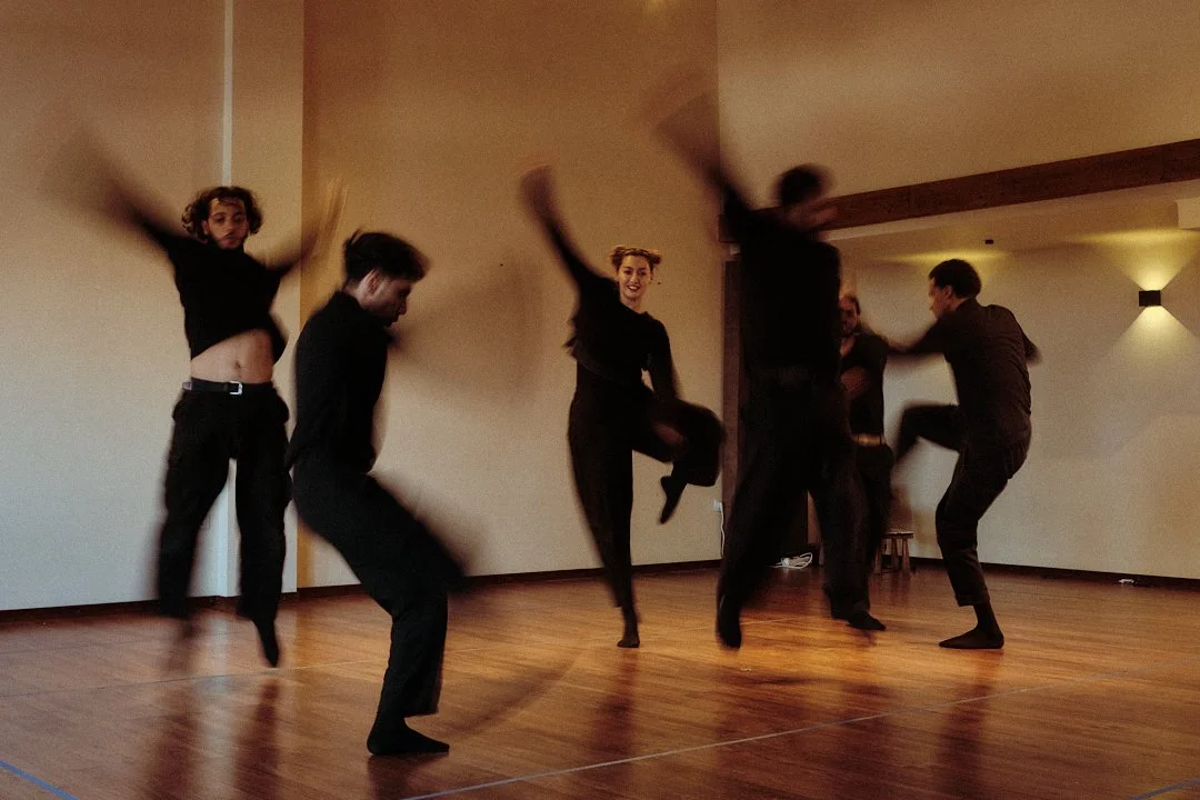 Groupe de danseurs en vêtements noirs répétant une chorégraphie dans un studio de danse.